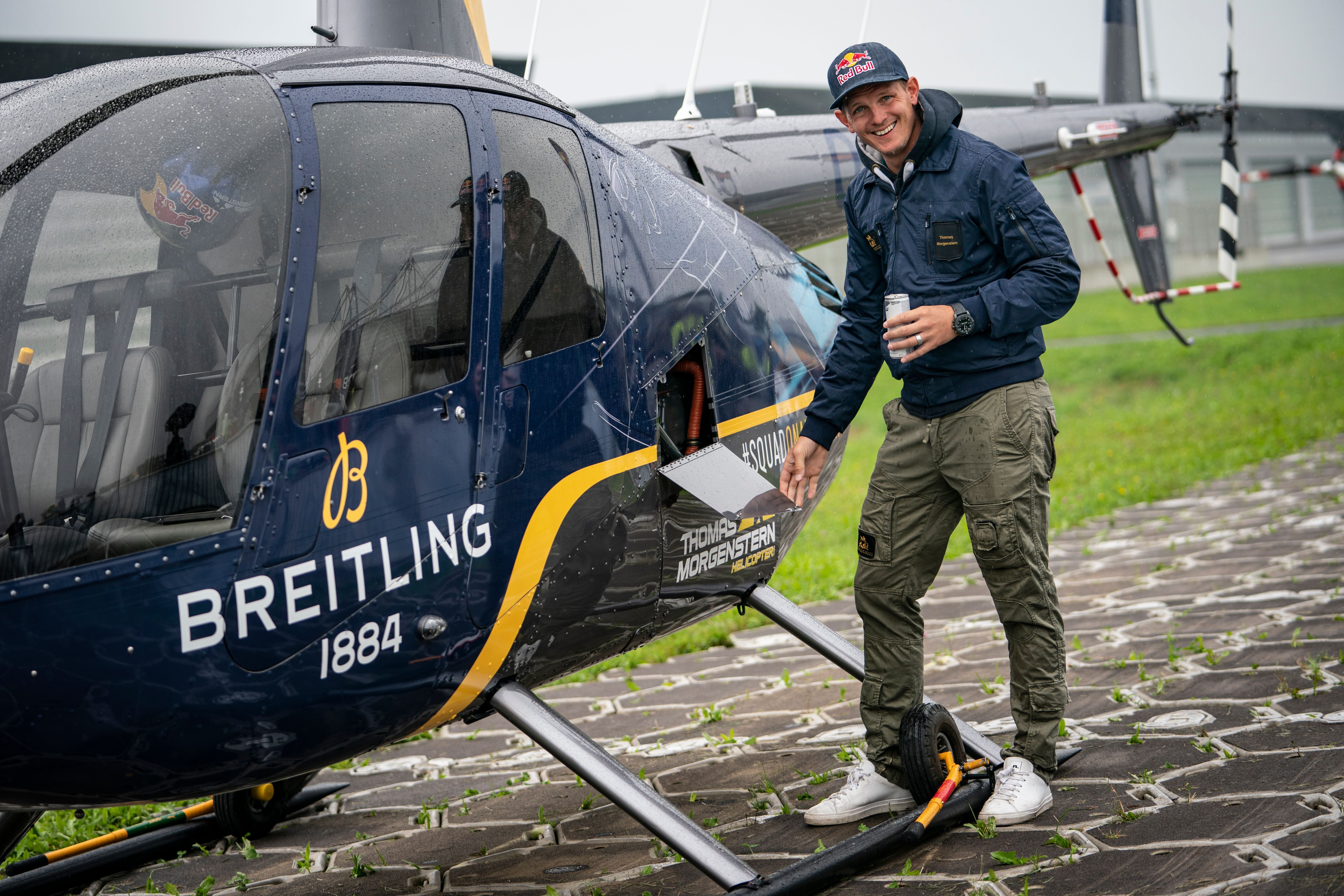 Mann steht neben einem Hubschrauber mit "Breitling" Logo und lächelt in die Kamera.