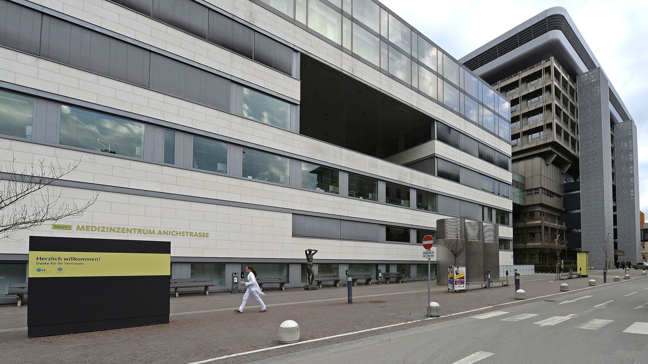 Moderne Außenansicht der Universitätsklinik Innsbruck mit Gehweg und einer Person in weißer Kleidung.