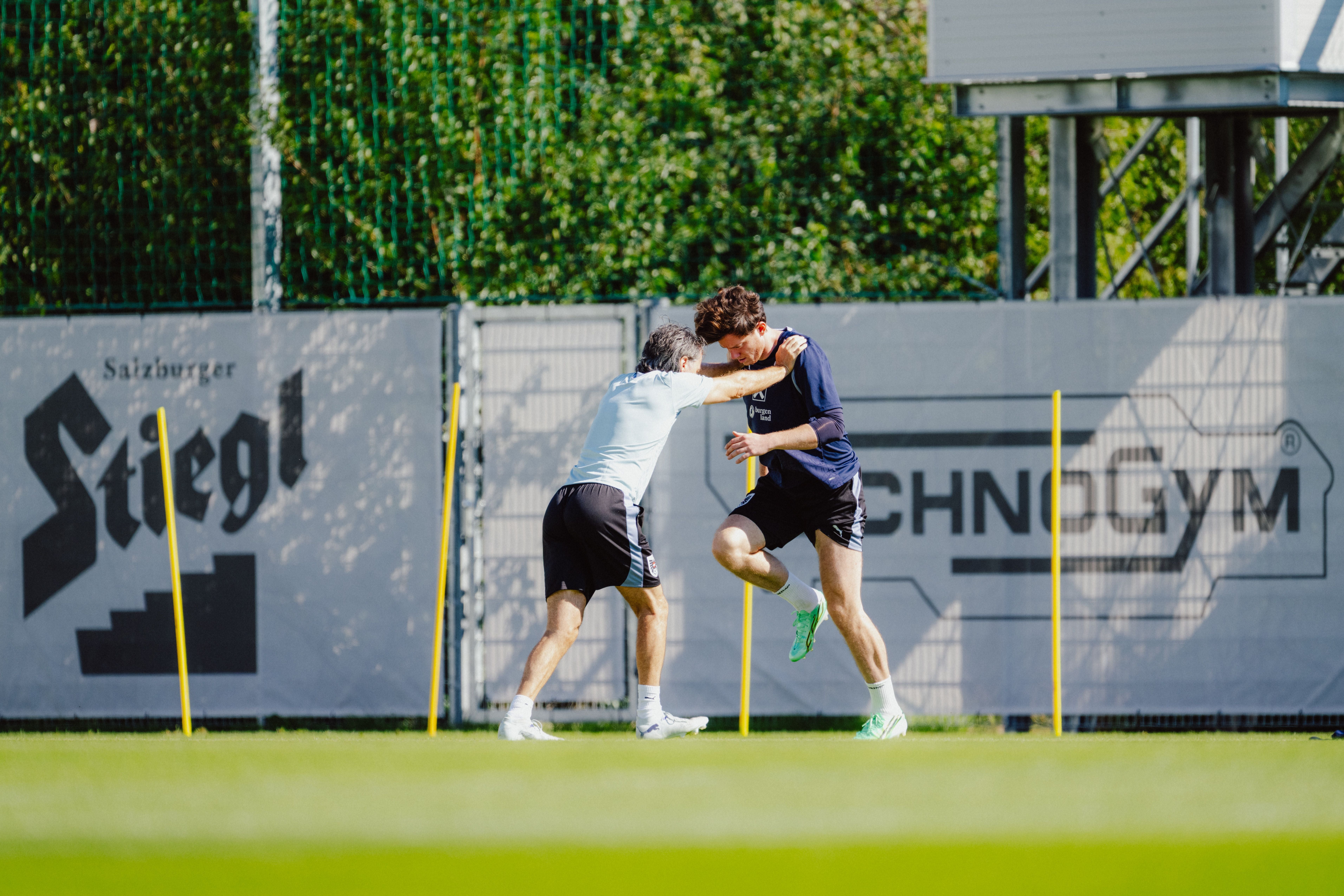 Zwei Fußballspieler trainieren auf dem Rasen zwischen gelben Stangen.