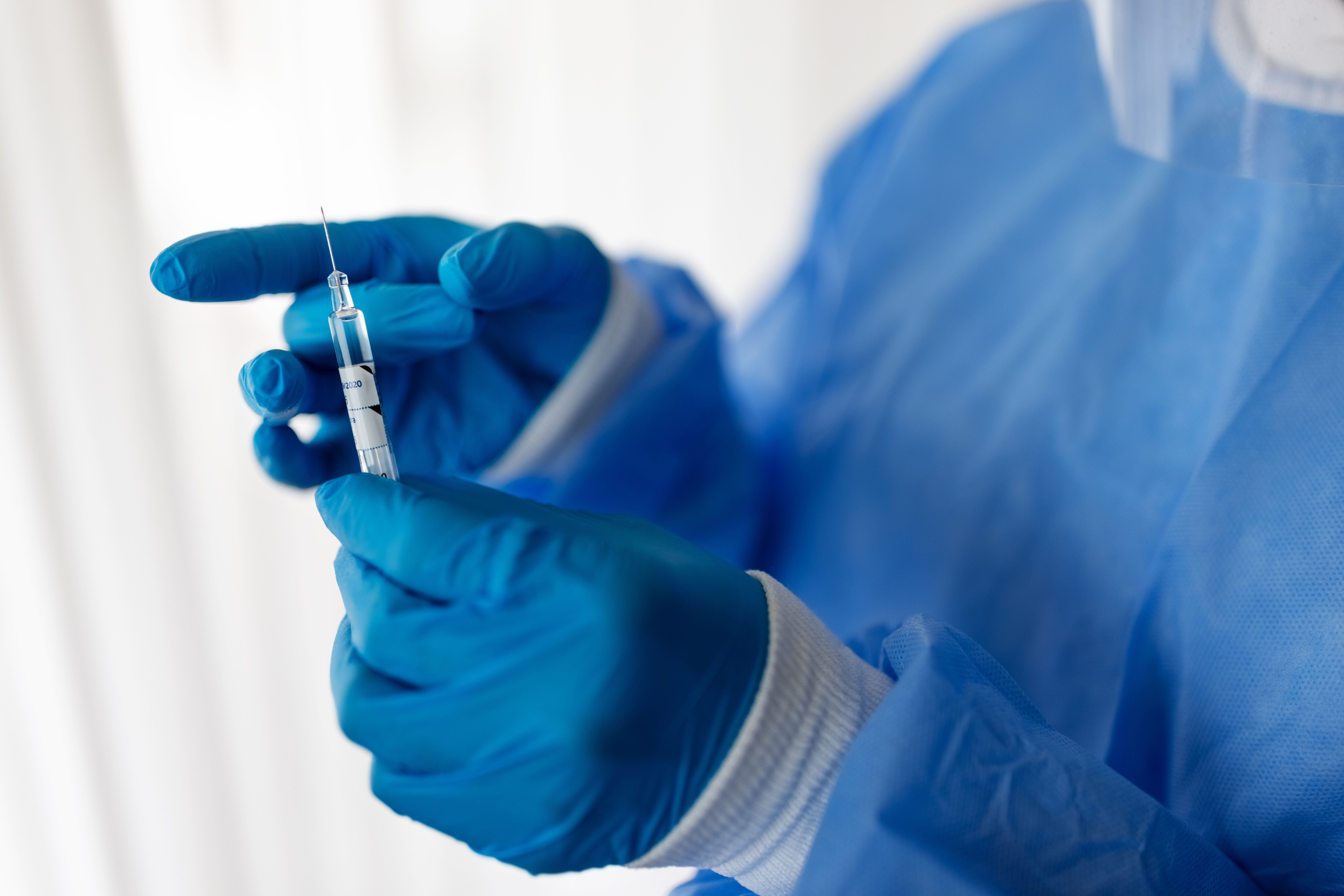 Nahaufnahme: Hände mit blauen Handschuhen bereiten eine Spritze mit Coronavirus-Impfstoff vor.