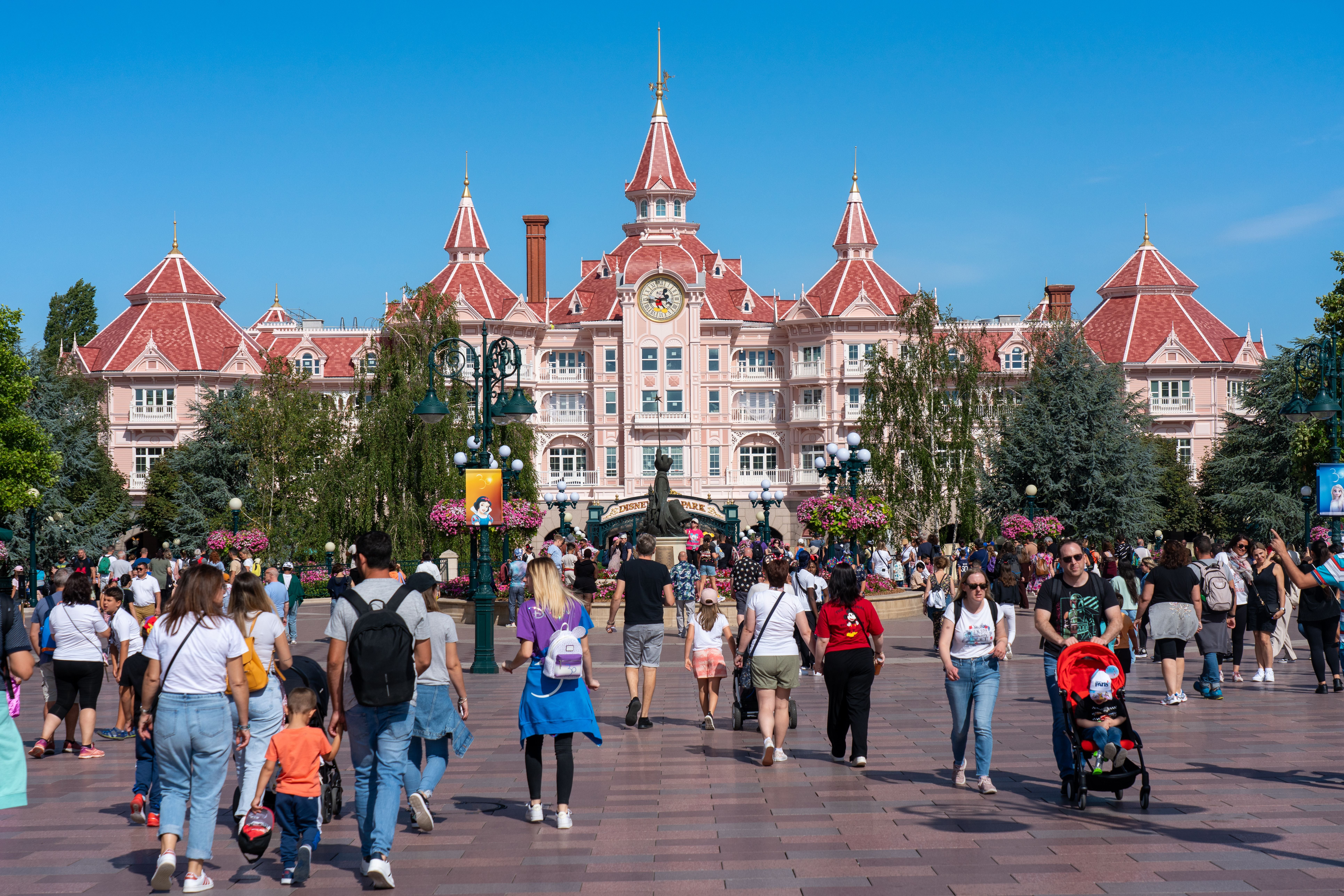 Menschen gehen bei sonnigem Wetter vor dem Disneyland Paris Hotel spazieren.