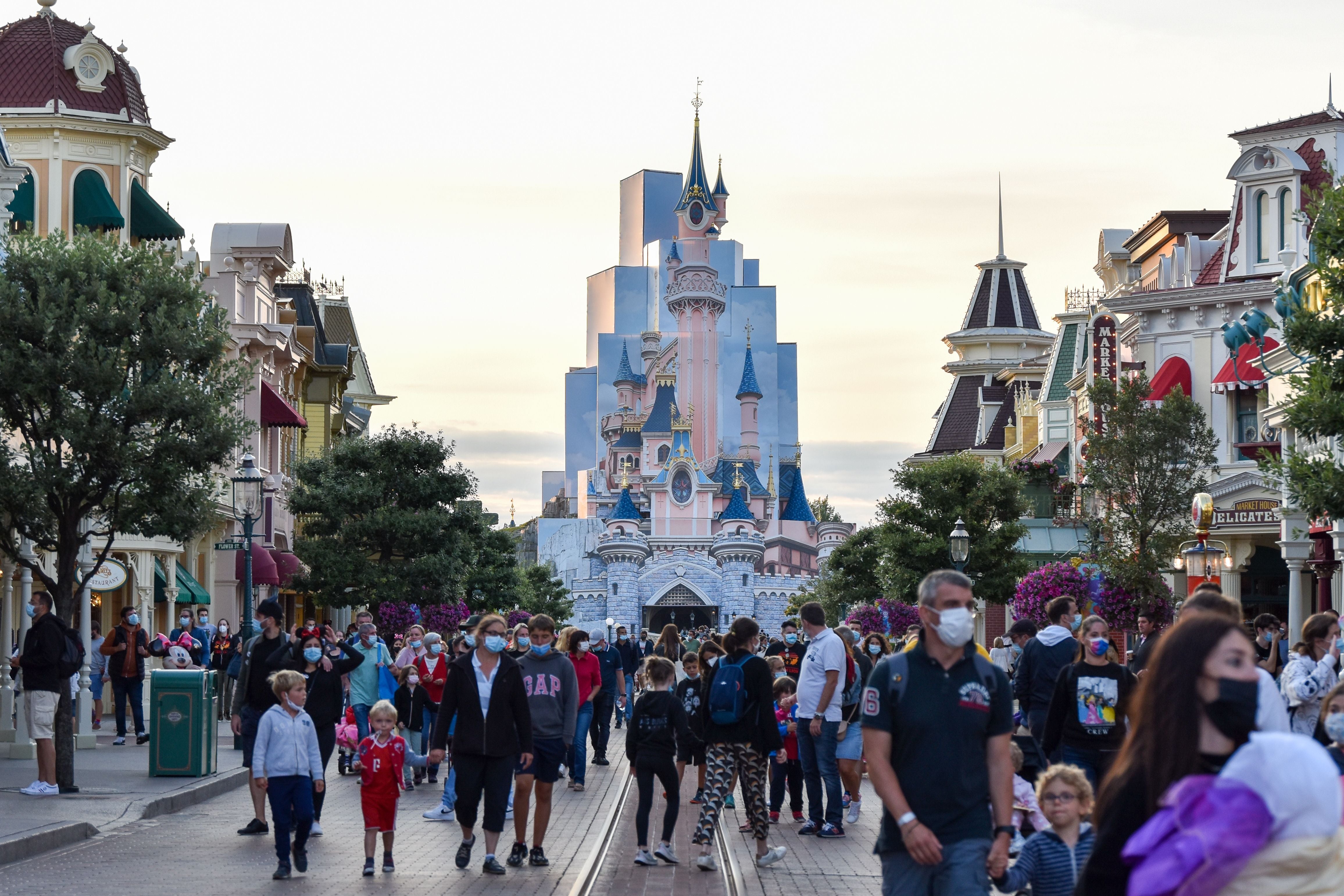 Viele Touristen mit Masken spazieren durch Disneyland Paris, das Schloss im Hintergrund.