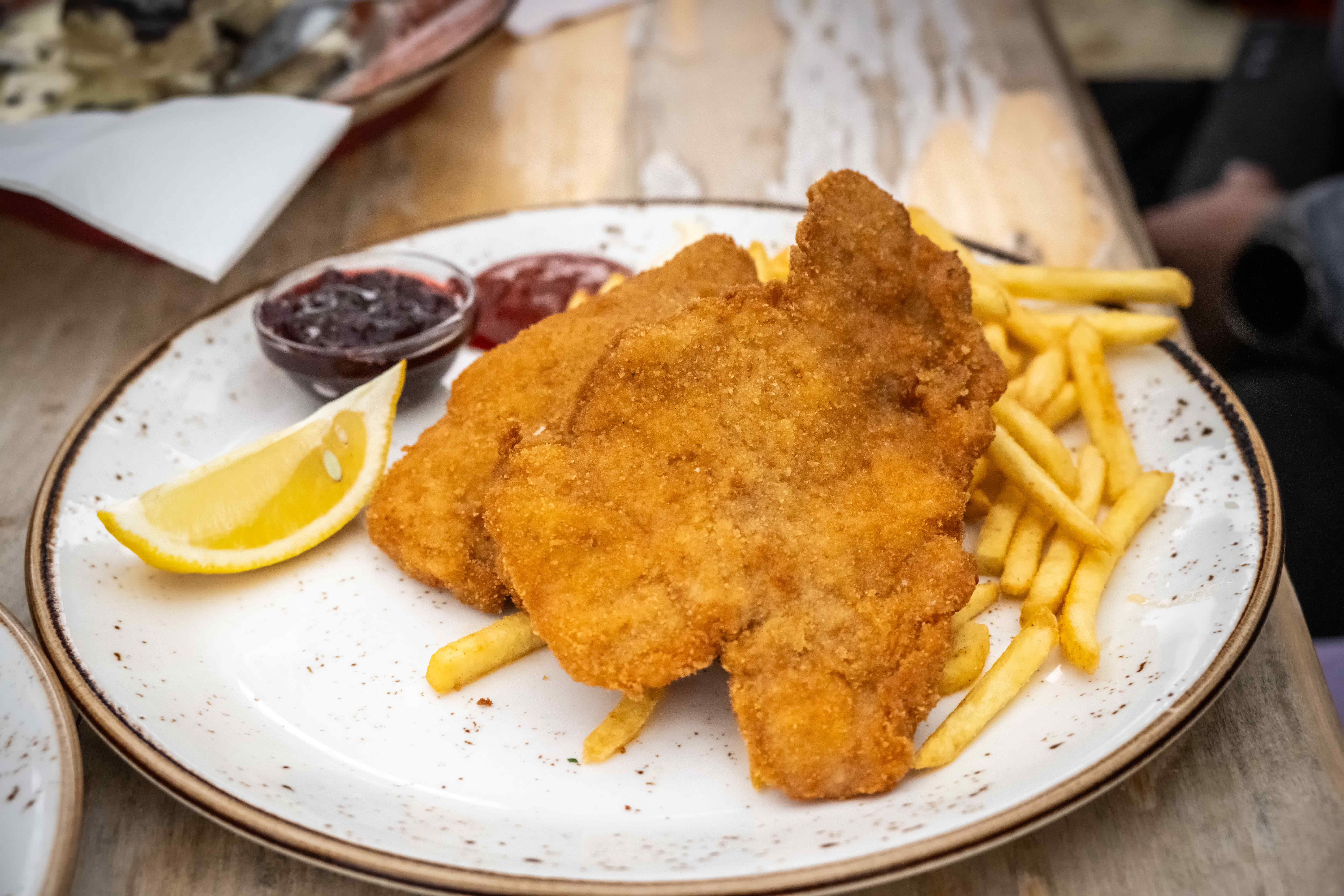 Schnitzel mit Pommes, Zitronenschnitz und zwei Soßen auf einem weißen Teller.