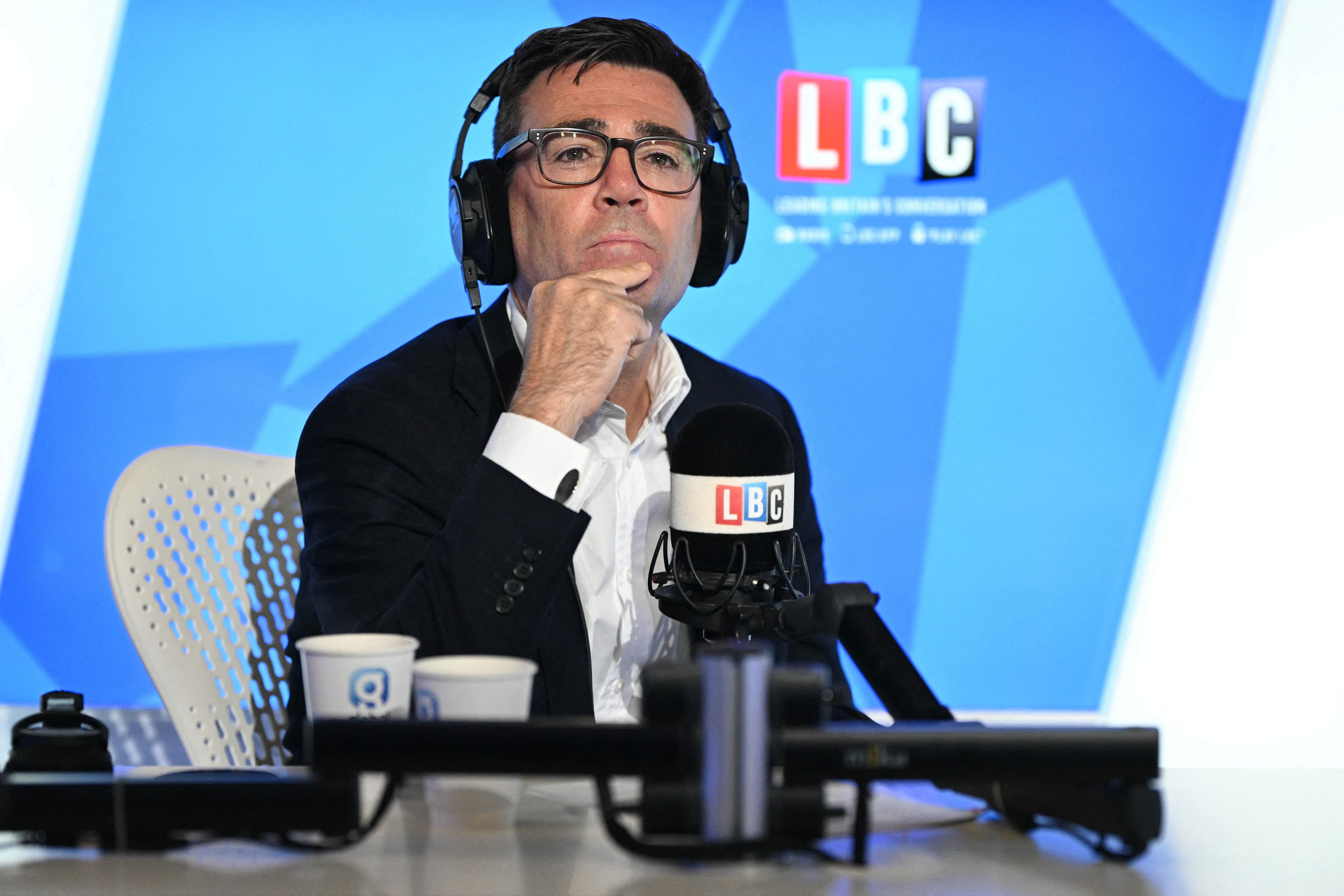 Mann mit Kopfhörern spricht ins Mikrofon beim Radiosender LBC, blauer Hintergrund.