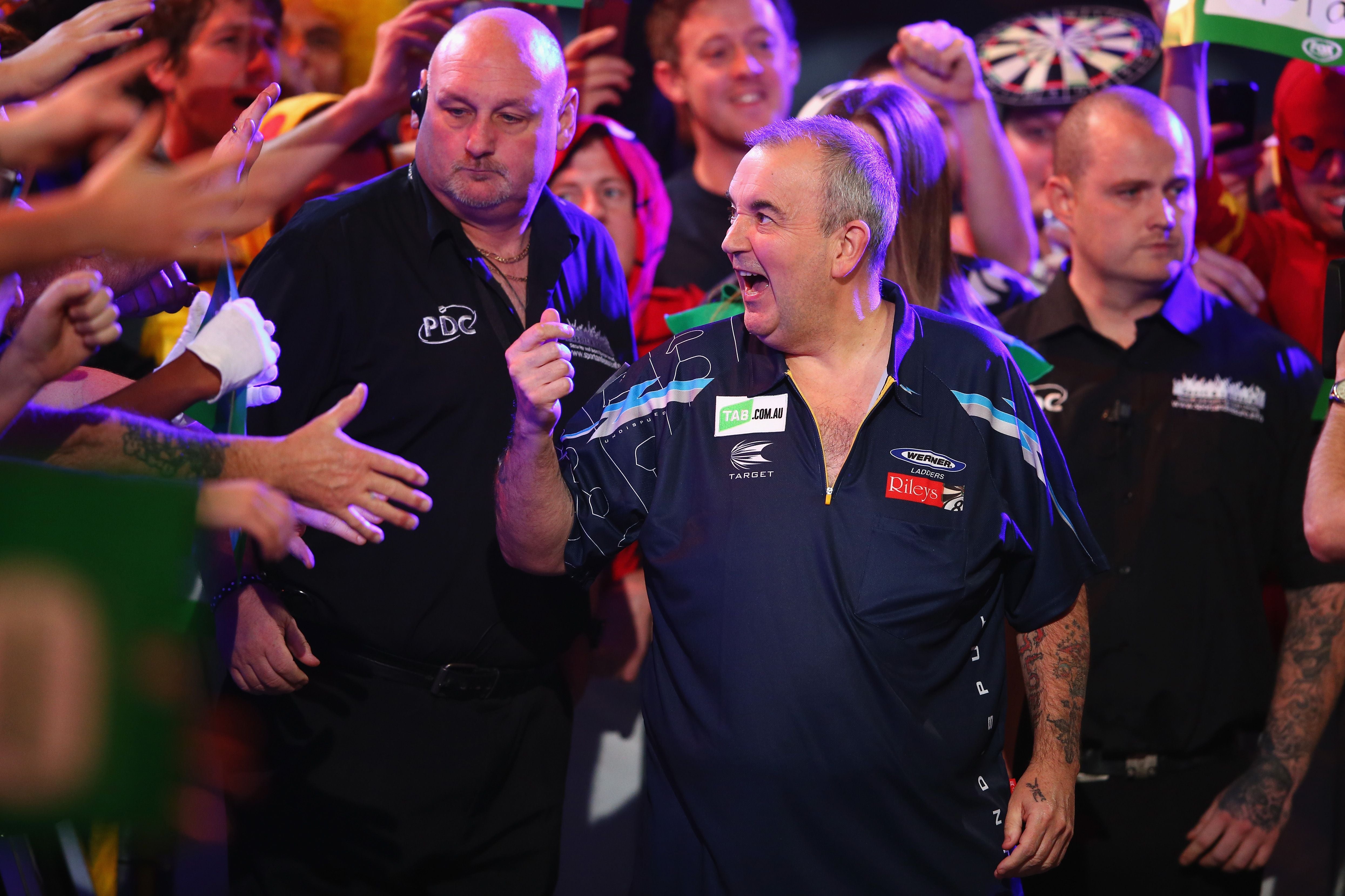 Ein Darts-Spieler jubelt auf dem Weg zur Bühne, umgeben von Fans und Sicherheitskräften.