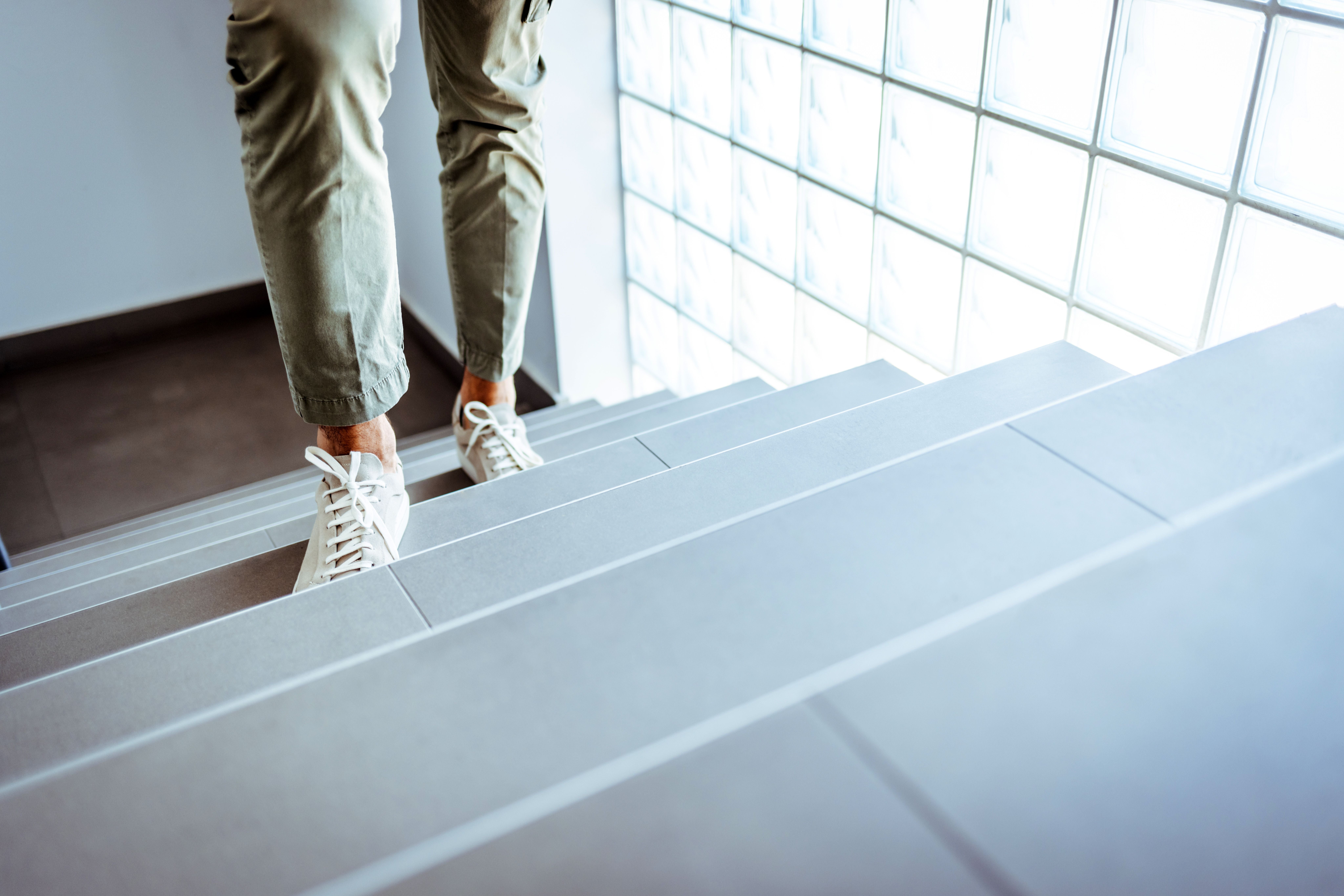 Person mit beigen Hosen und weißen Sneakern geht eine moderne Treppe hinauf.