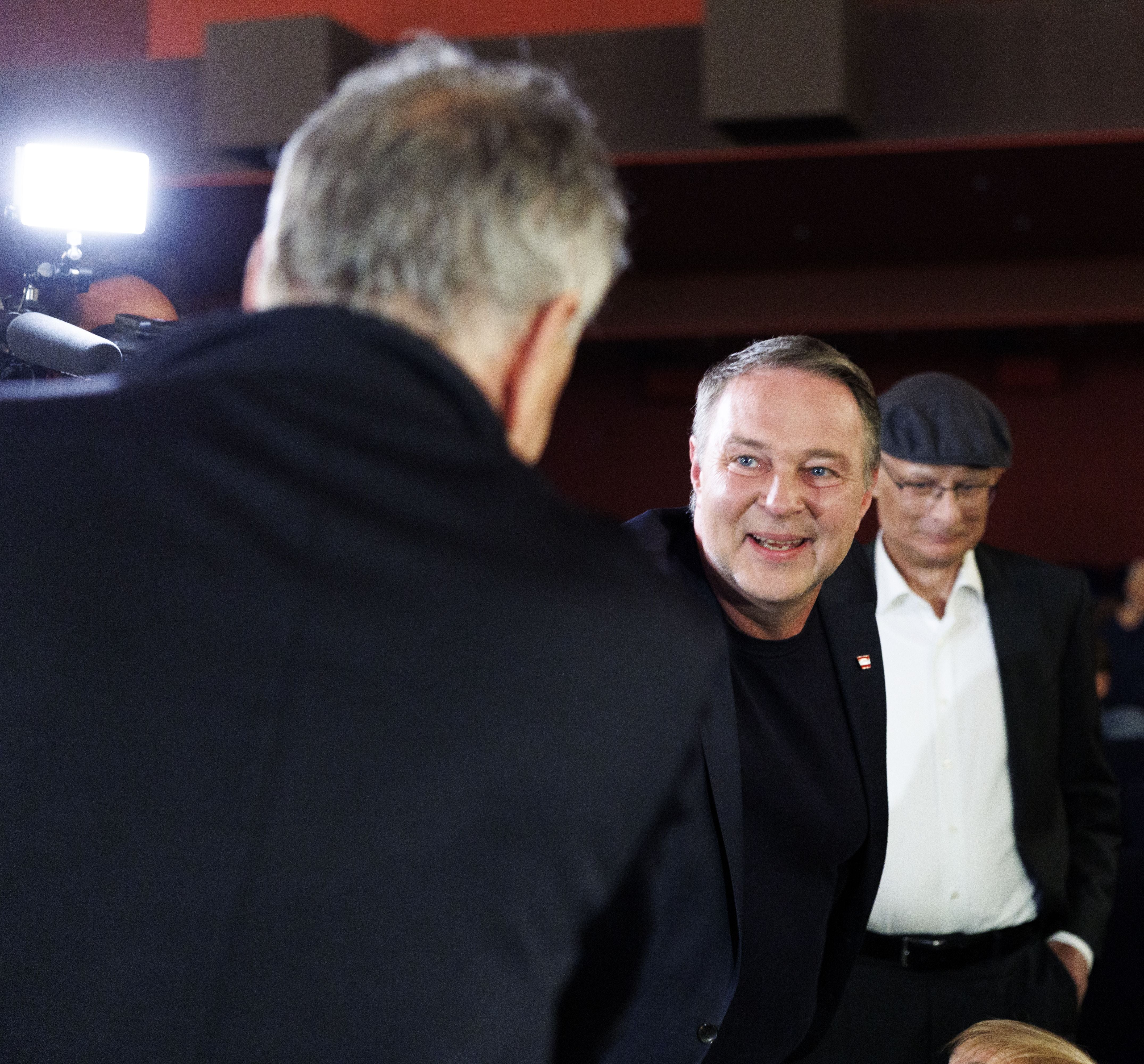 Drei Männer in Anzügen unterhalten sich bei einer Filmpremiere im Kino.