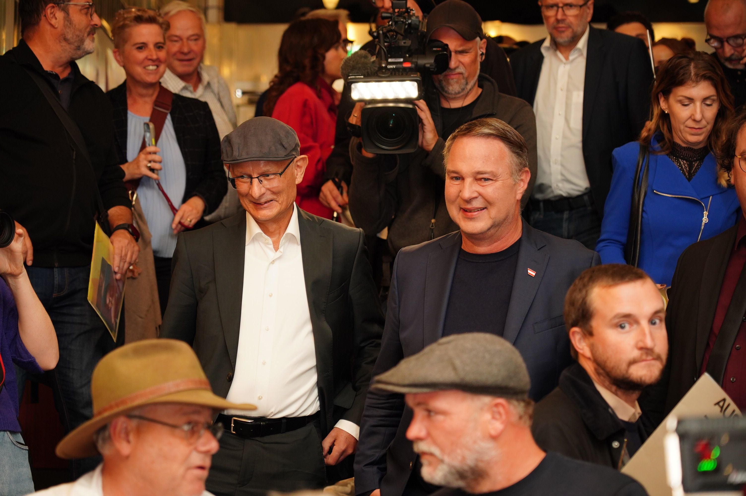 Andreas Babler neben Markus Marterbauer inmitten einer Gruppe von Menschen, Presse im Hintergrund.