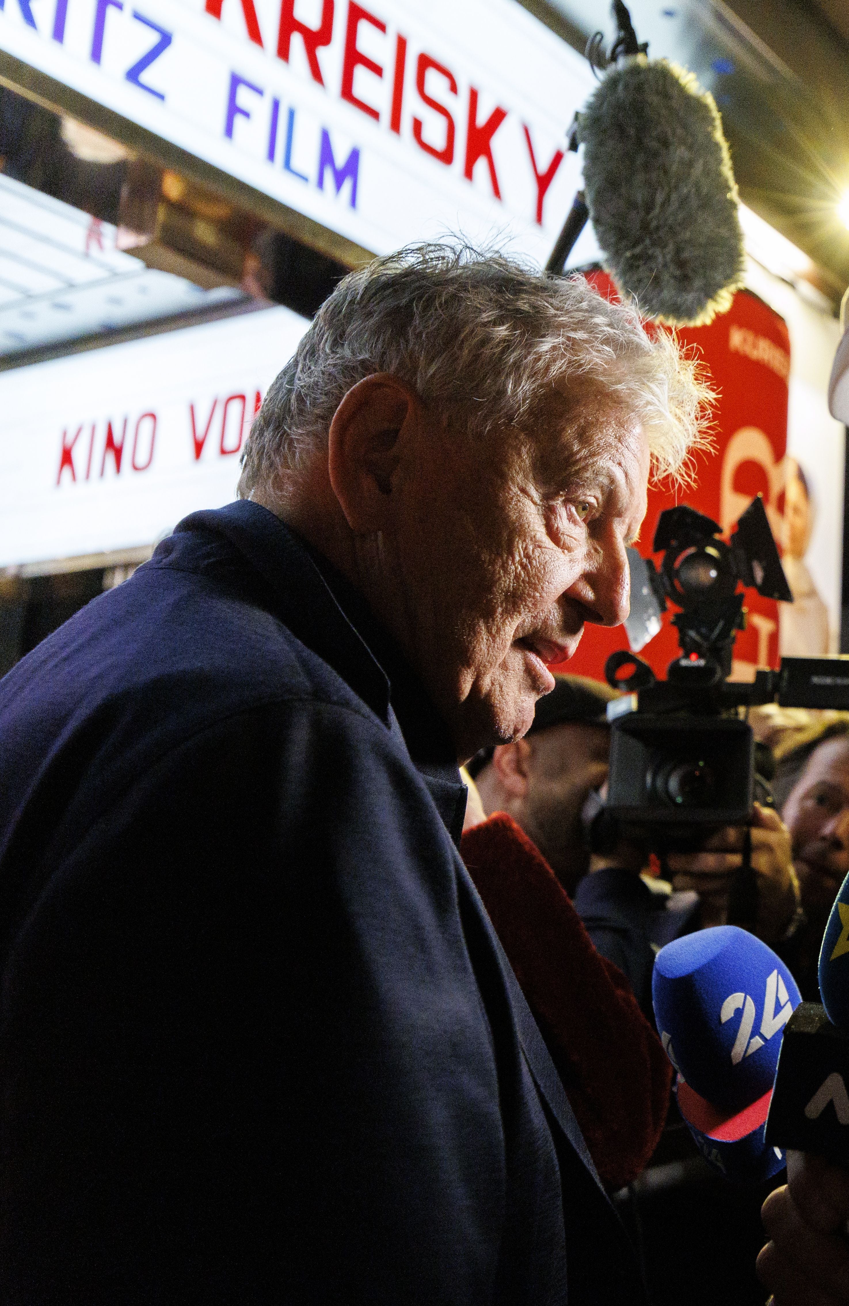 Ein älterer Mann wird bei einer Filmpremiere im Gartenbaukino von Kameras und Mikrofonen umringt.