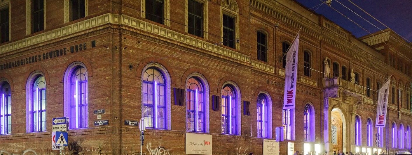 Backsteingebäude des WUK in Wien mit lila beleuchteten Fenstern bei Nacht.