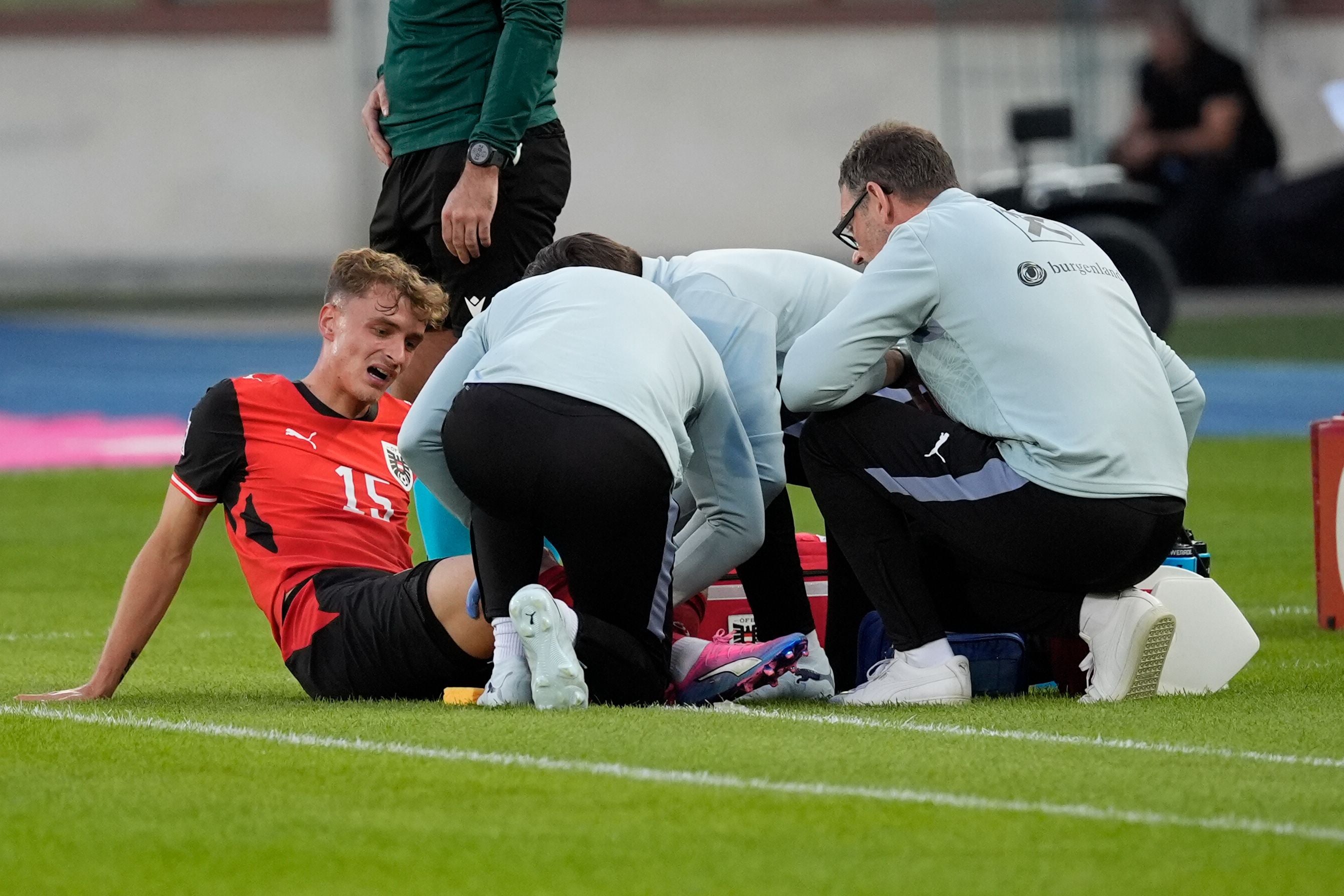 Ein Fußballspieler sitzt verletzt am Spielfeldrand, Betreuer kümmern sich um ihn.