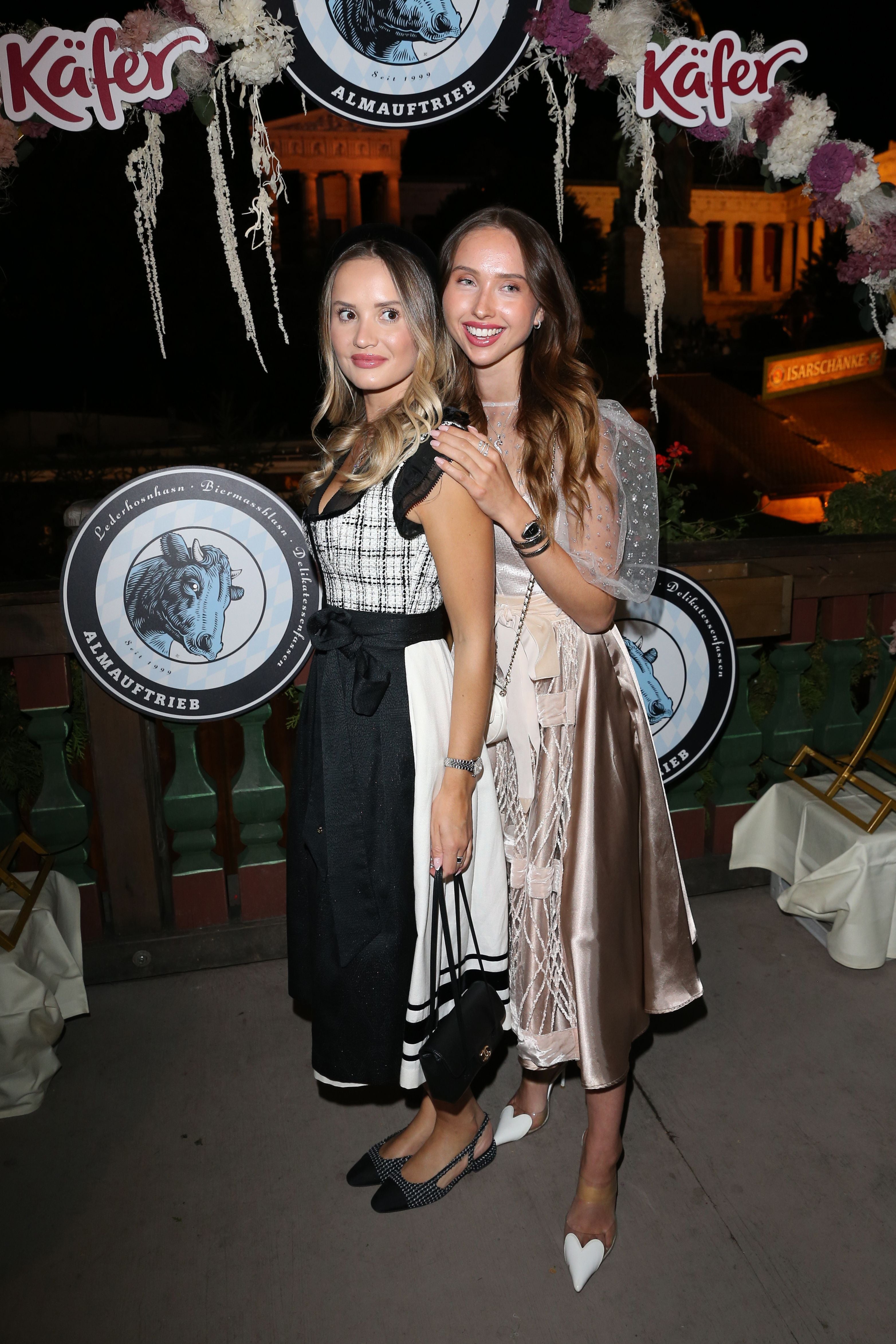 Zwei junge Frauen in festlicher Tracht posieren lächelnd bei einer Oktoberfest-Veranstaltung.