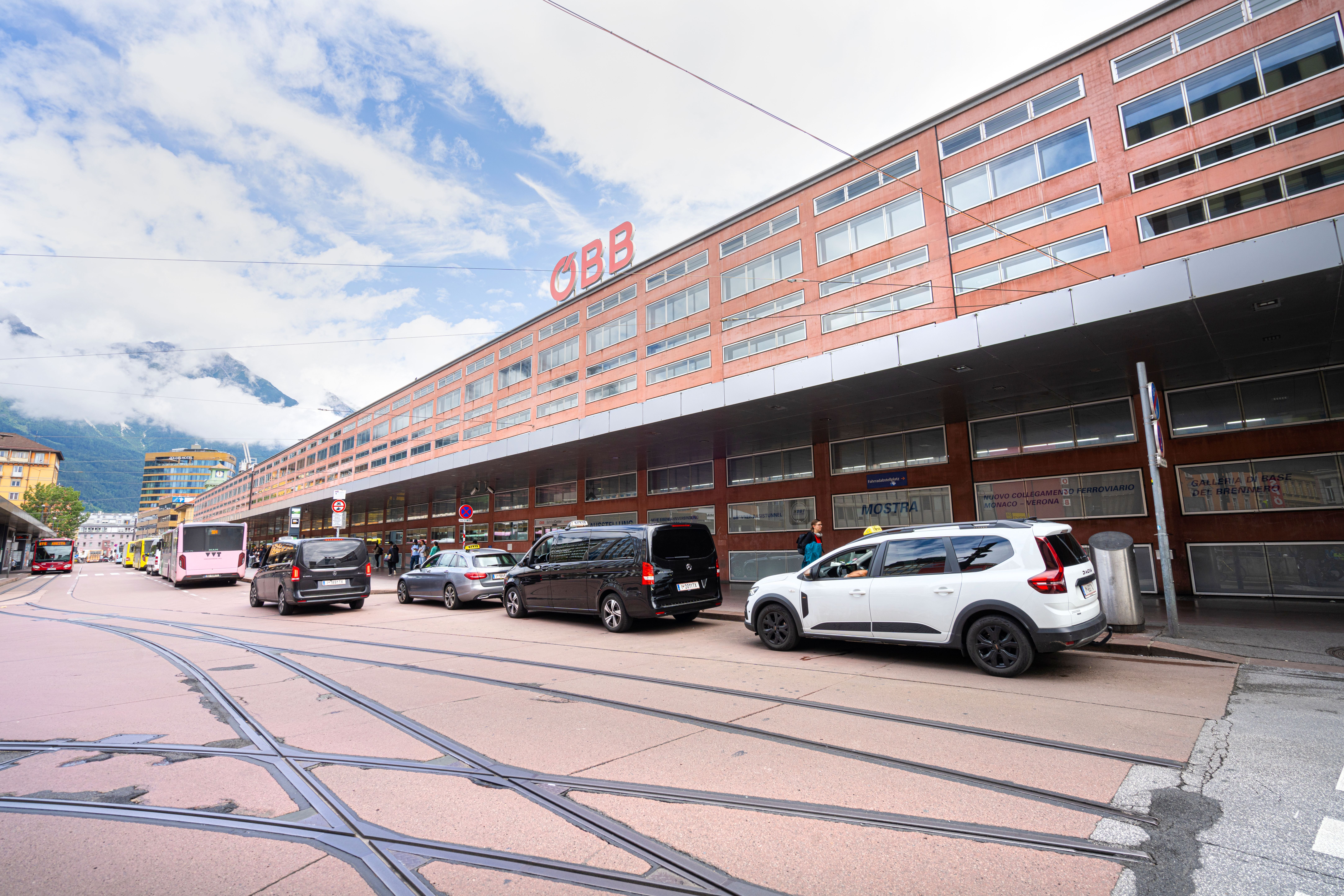 Außenansicht des Innsbrucker Hauptbahnhofs mit Taxis und Bussen davor bei Tageslicht.