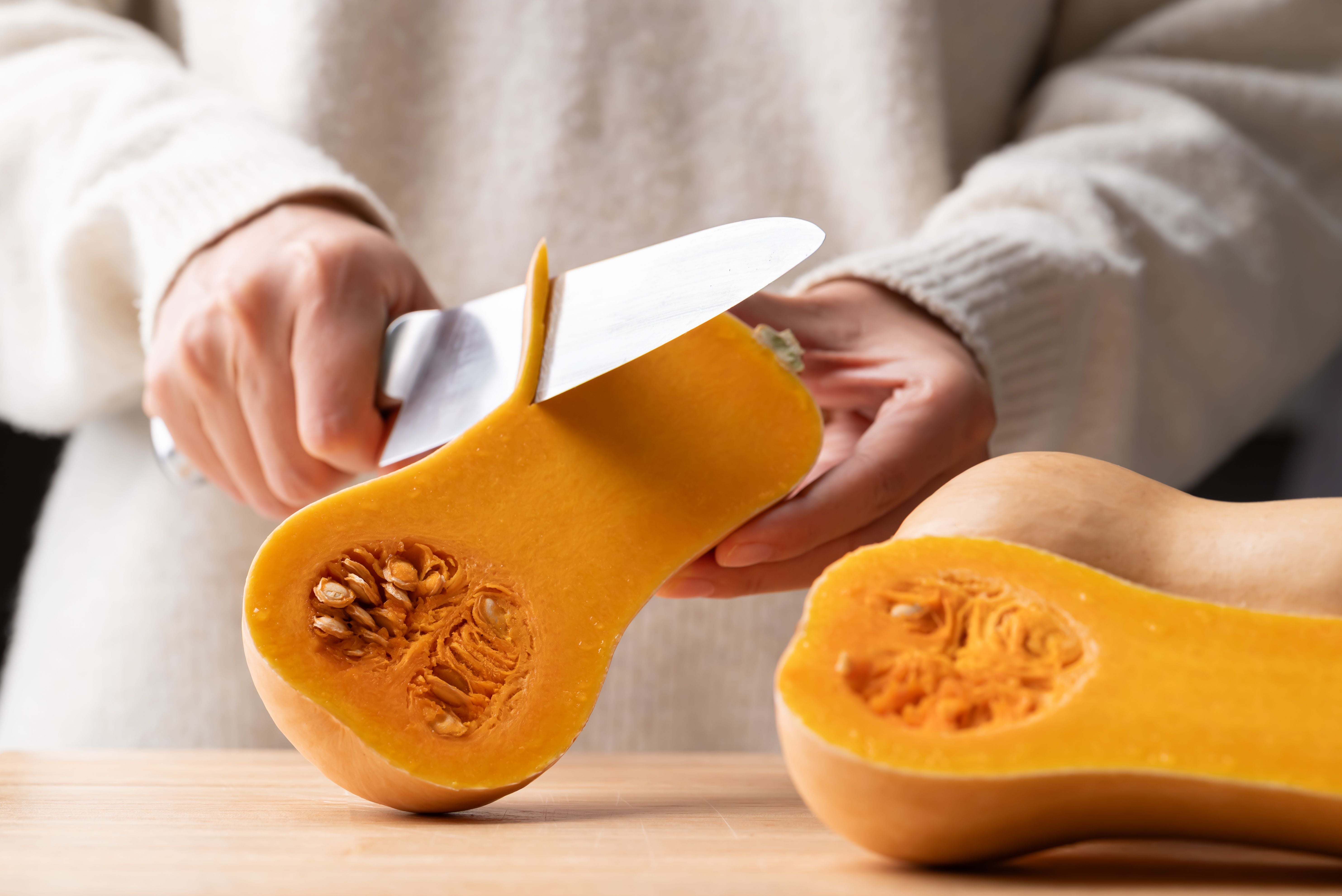 Person schneidet einen Butternutkürbis auf einem Holzbrett mit einem Küchenmesser.