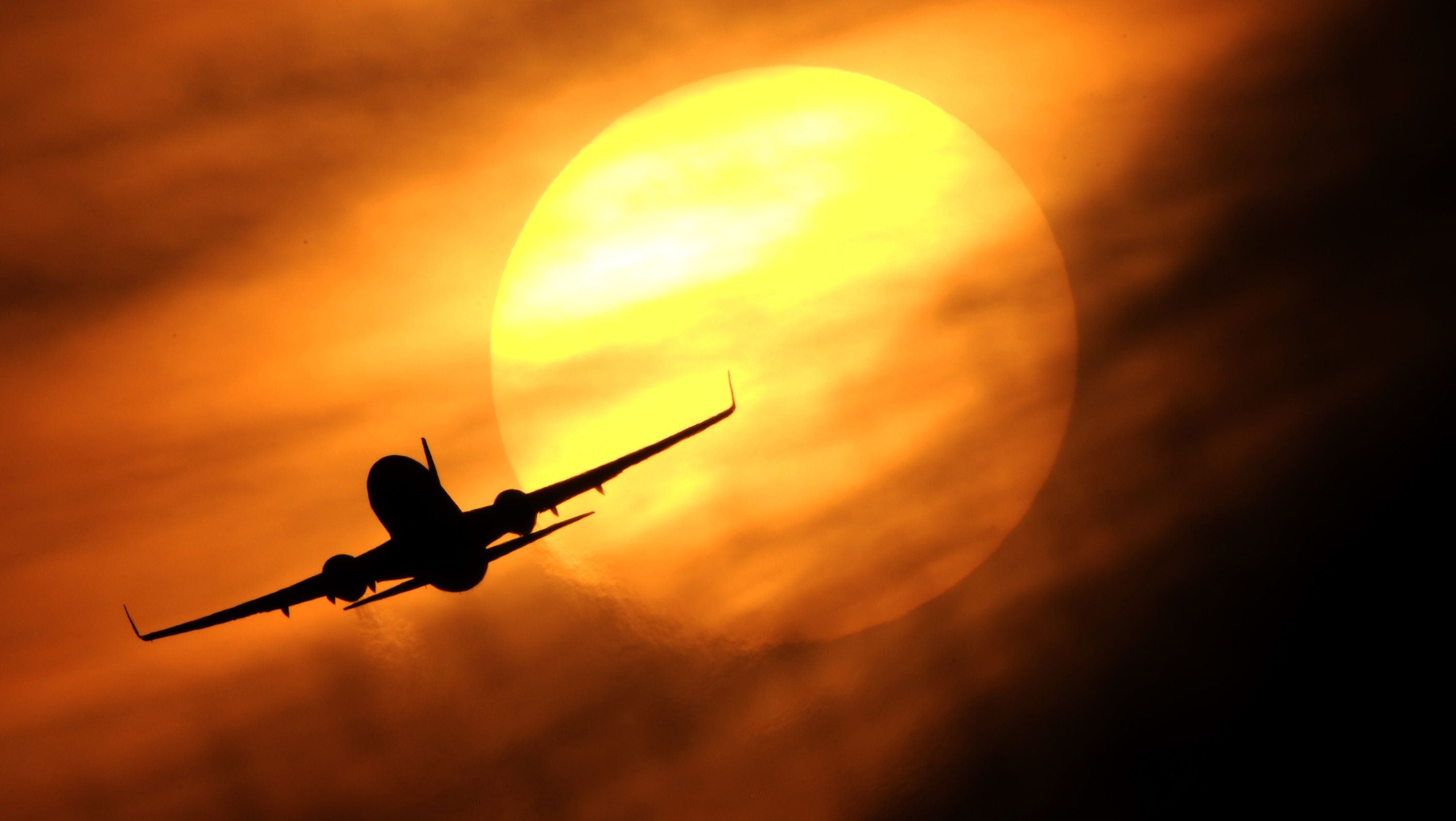 Silhouette eines Flugzeugs vor untergehender Sonne mit orangefarbenem Himmel.