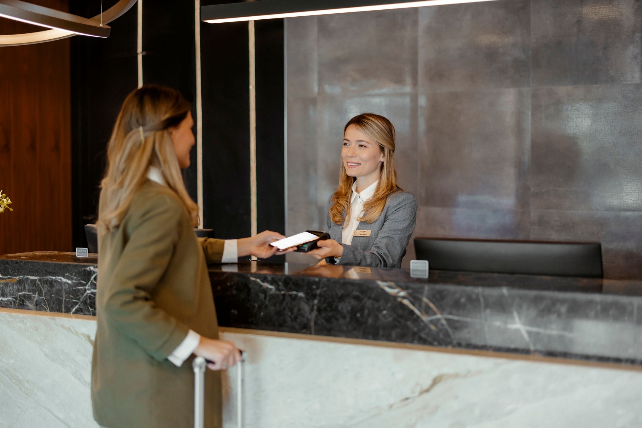 Frau bezahlt mit Handy per NFC-Technologie an der Hotelrezeption.