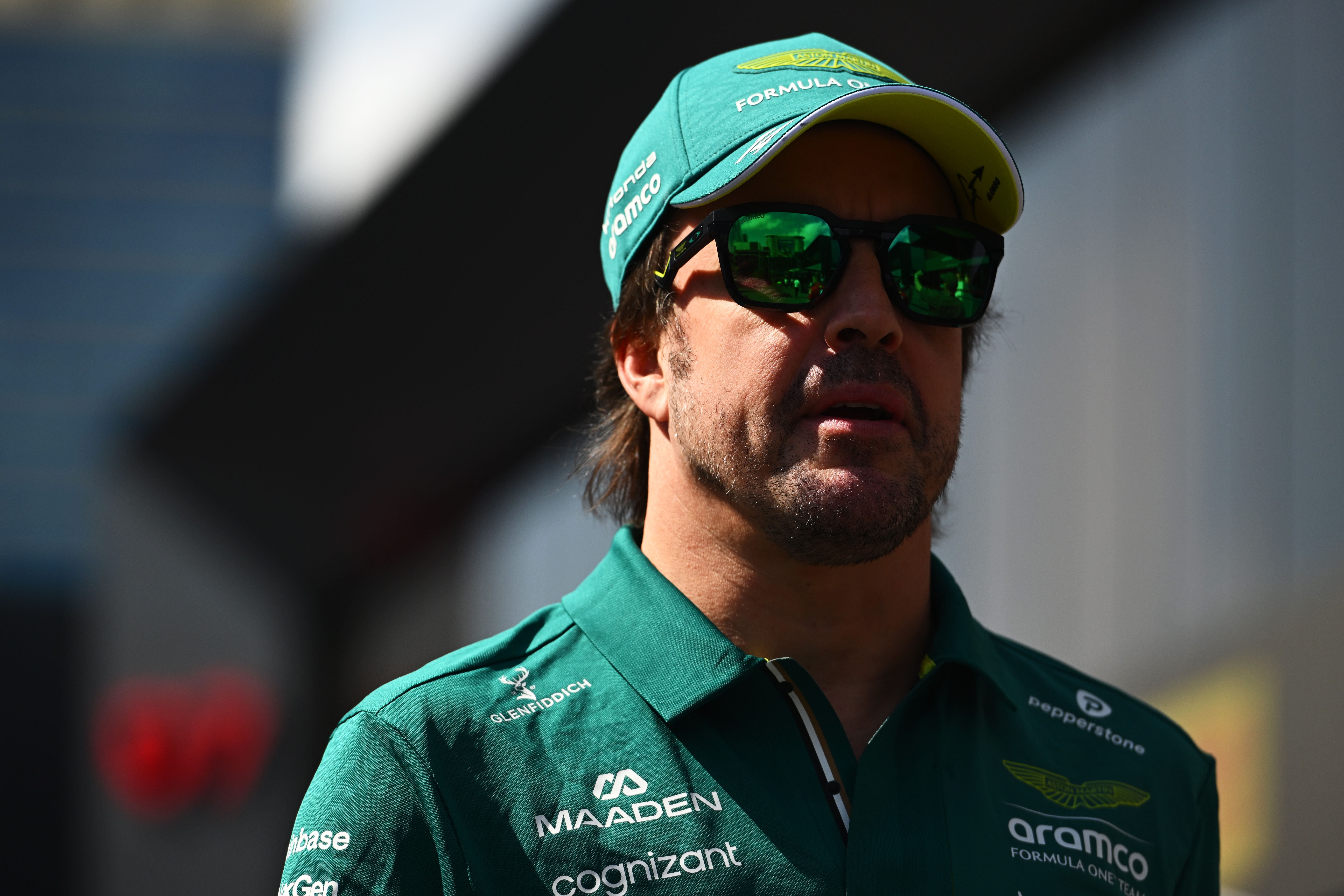 Ein Mann im grünen Aston-Martin-Shirt und -Basecap trägt eine Sonnenbrille im Sonnenlicht.