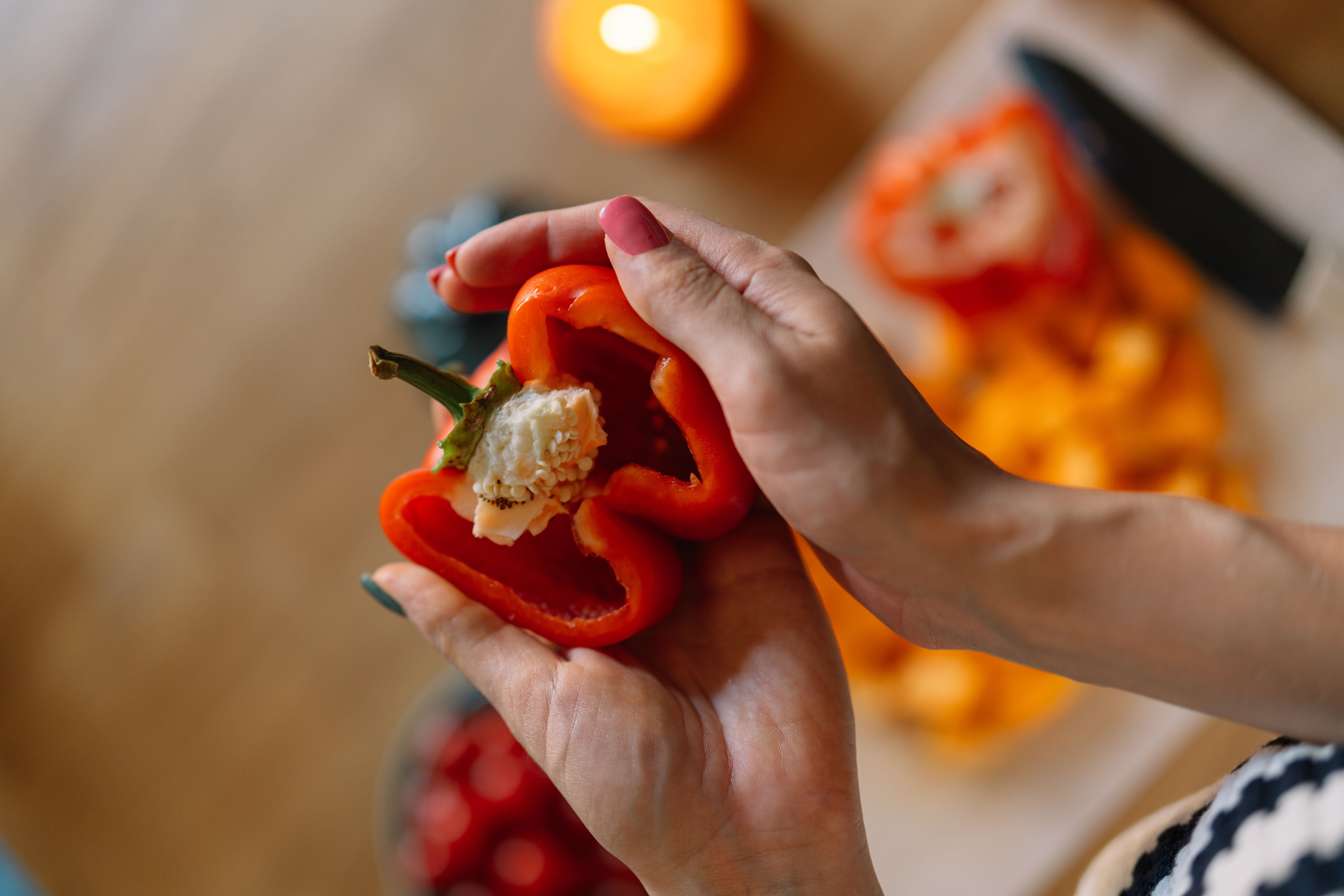 Zwei Hände halten eine aufgeschnittene rote Paprika über einem Küchentisch.