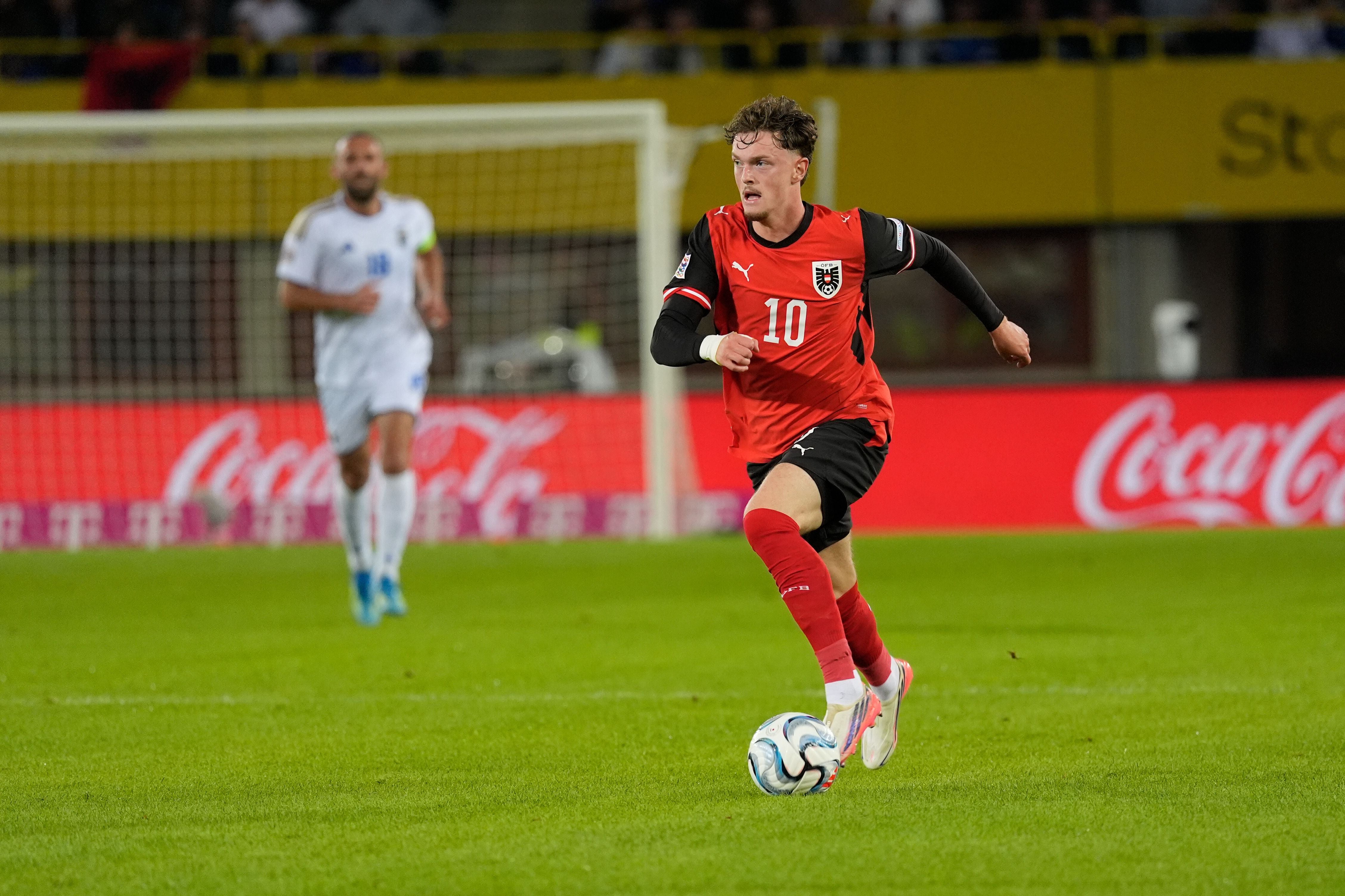 Ein österreichischer Fußballspieler im roten Trikot dribbelt den Ball auf dem Spielfeld.