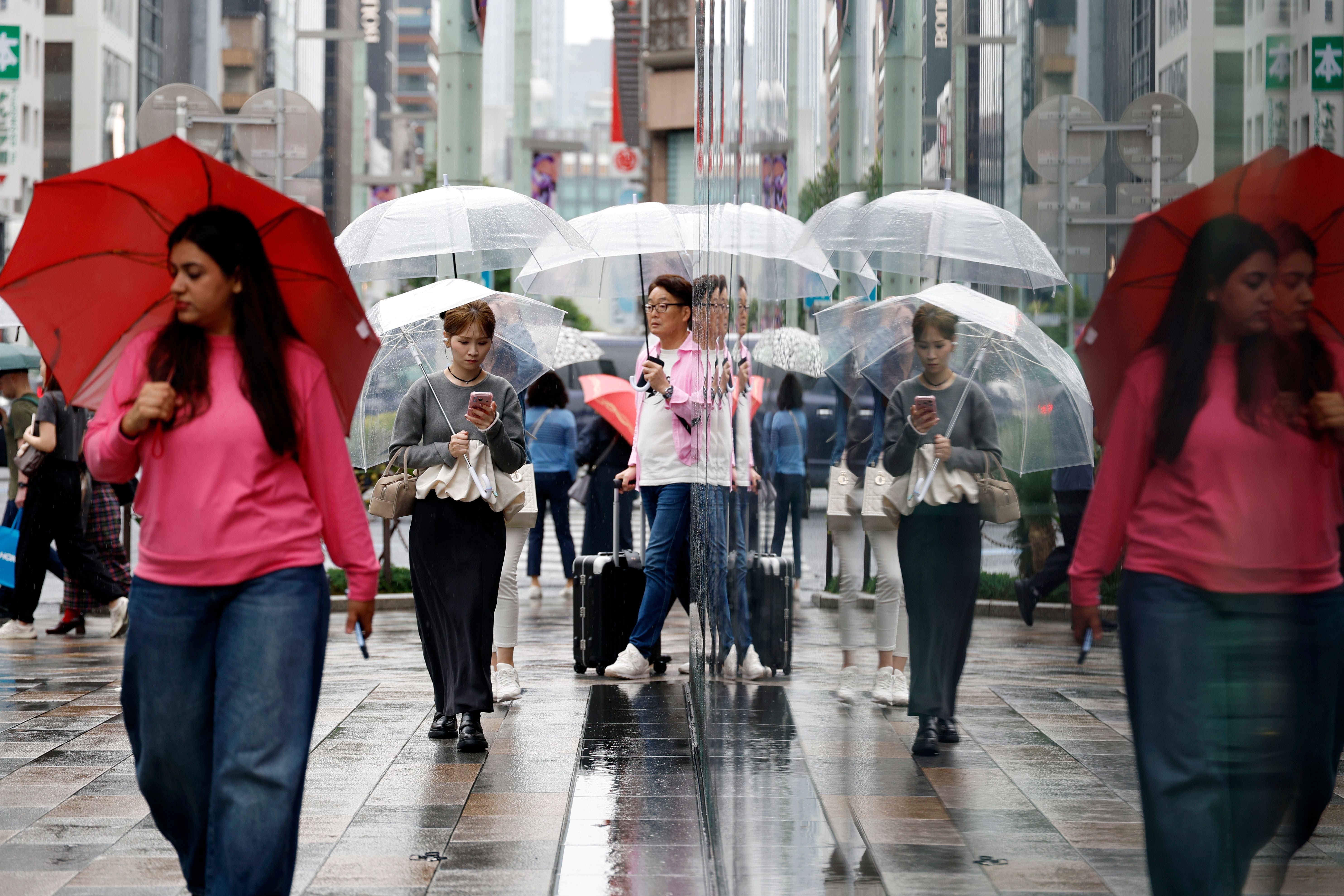 Menschen mit Regenschirmen laufen bei Regen durch die Ginza-Einkaufsstraße in Tokio.