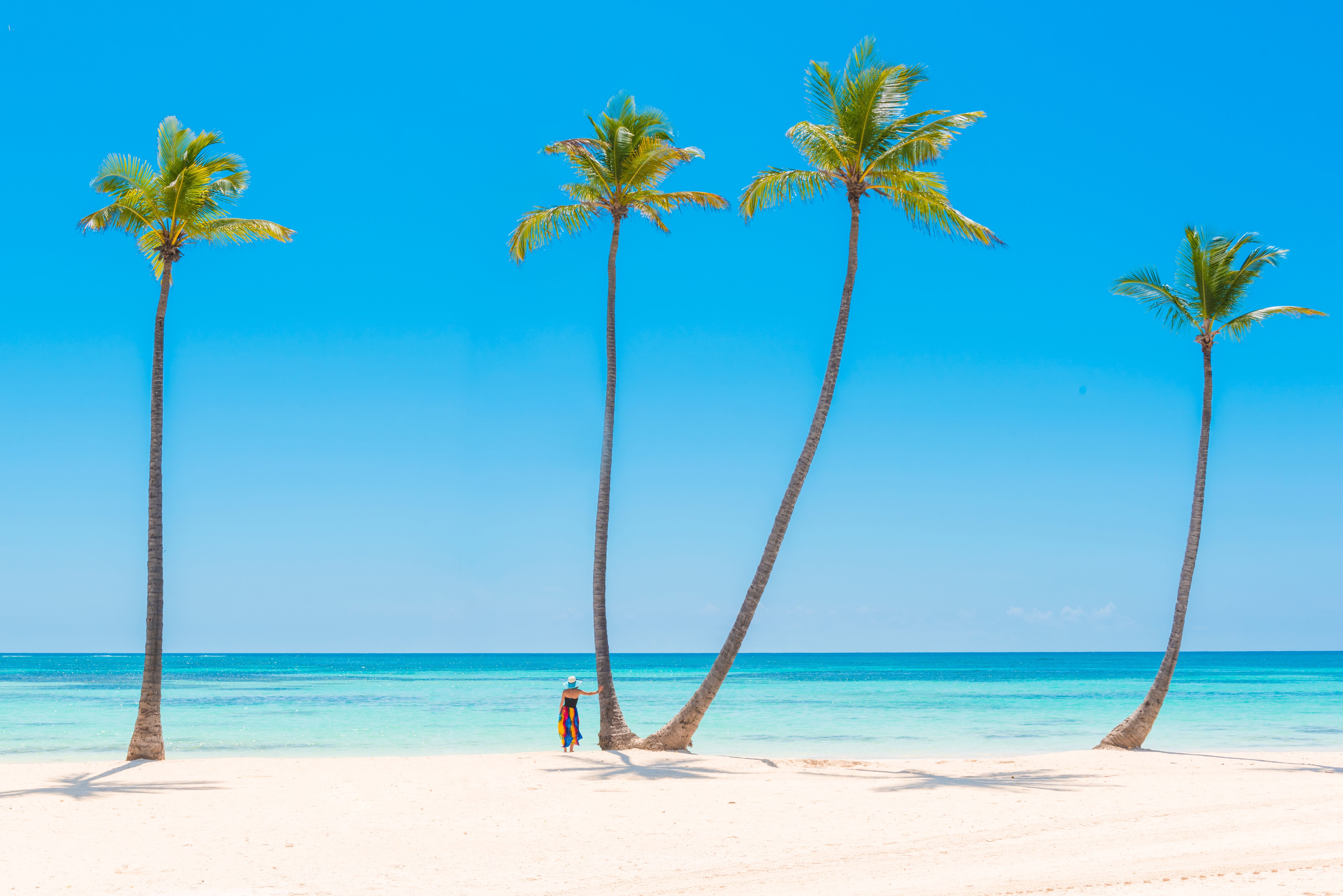 Frau steht unter hohen Palmen am weißen Sandstrand von Playa Juanillo, Punta Cana.