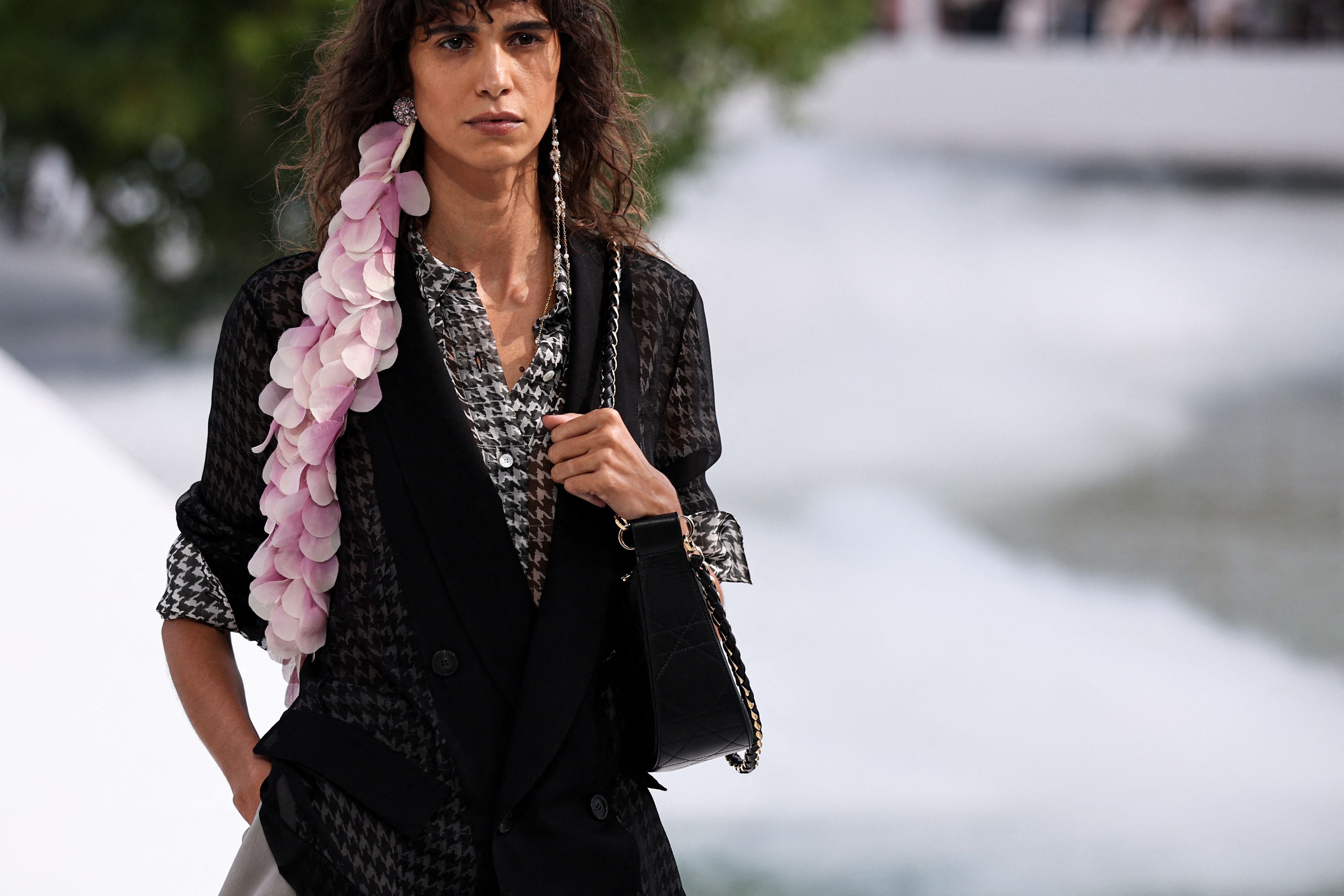 Model mit schwarz gemusterter Jacke und rosafarbenem Blumendetail auf dem Laufsteg.