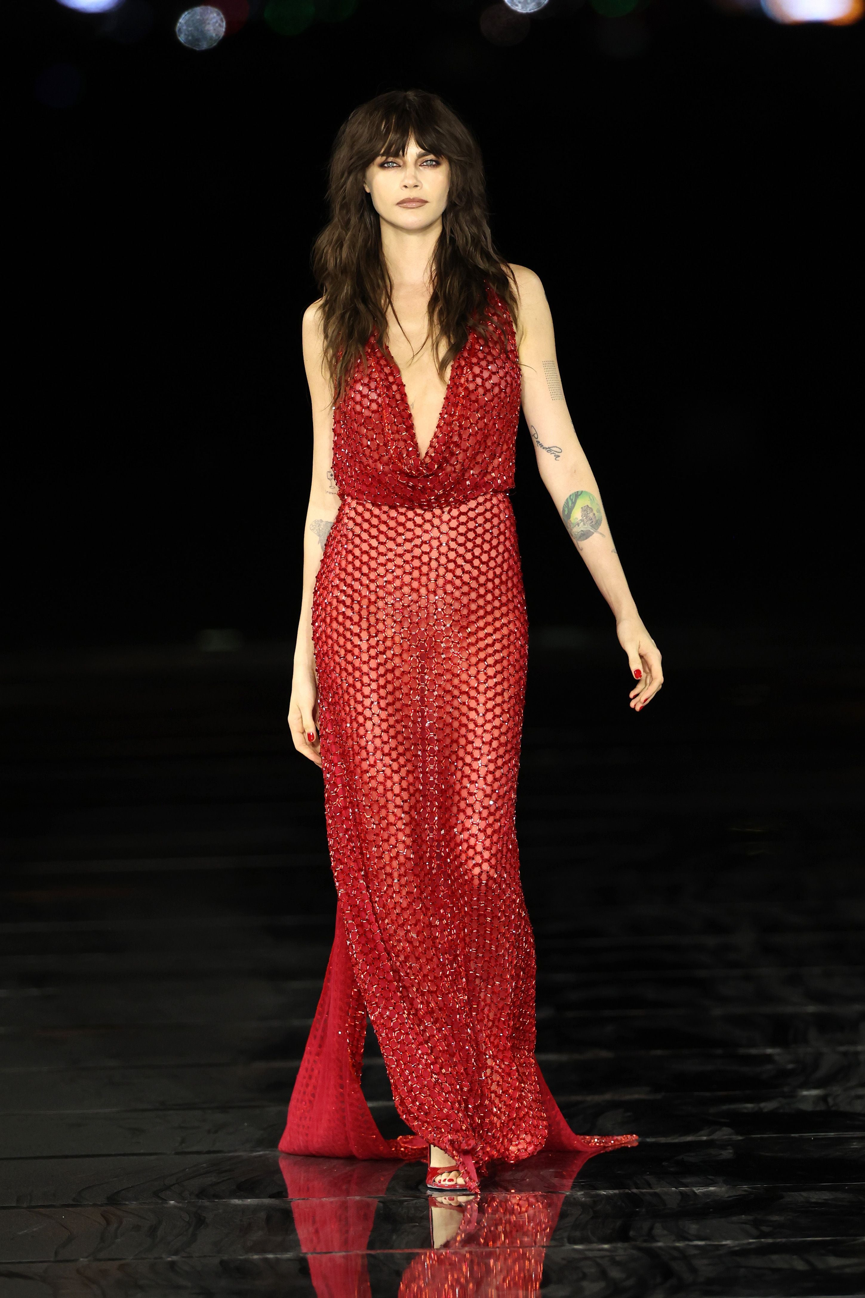 Model in langem, roten, glitzernden Kleid läuft auf dem Laufsteg vor dunklem Hintergrund.