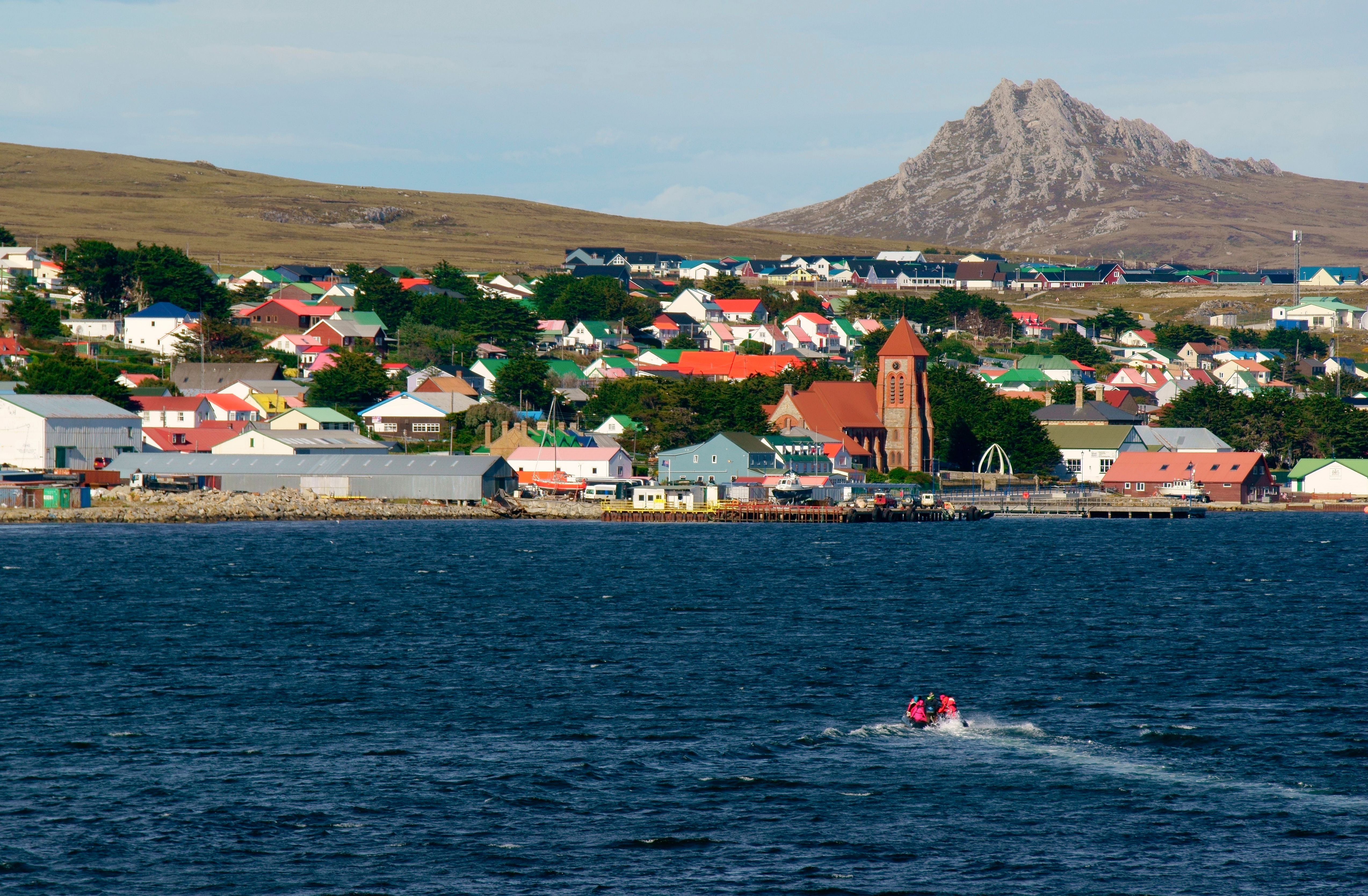 Blick auf Port Stanley mit bunten Häusern und Kirche am Wasser, im Hintergrund Hügel.