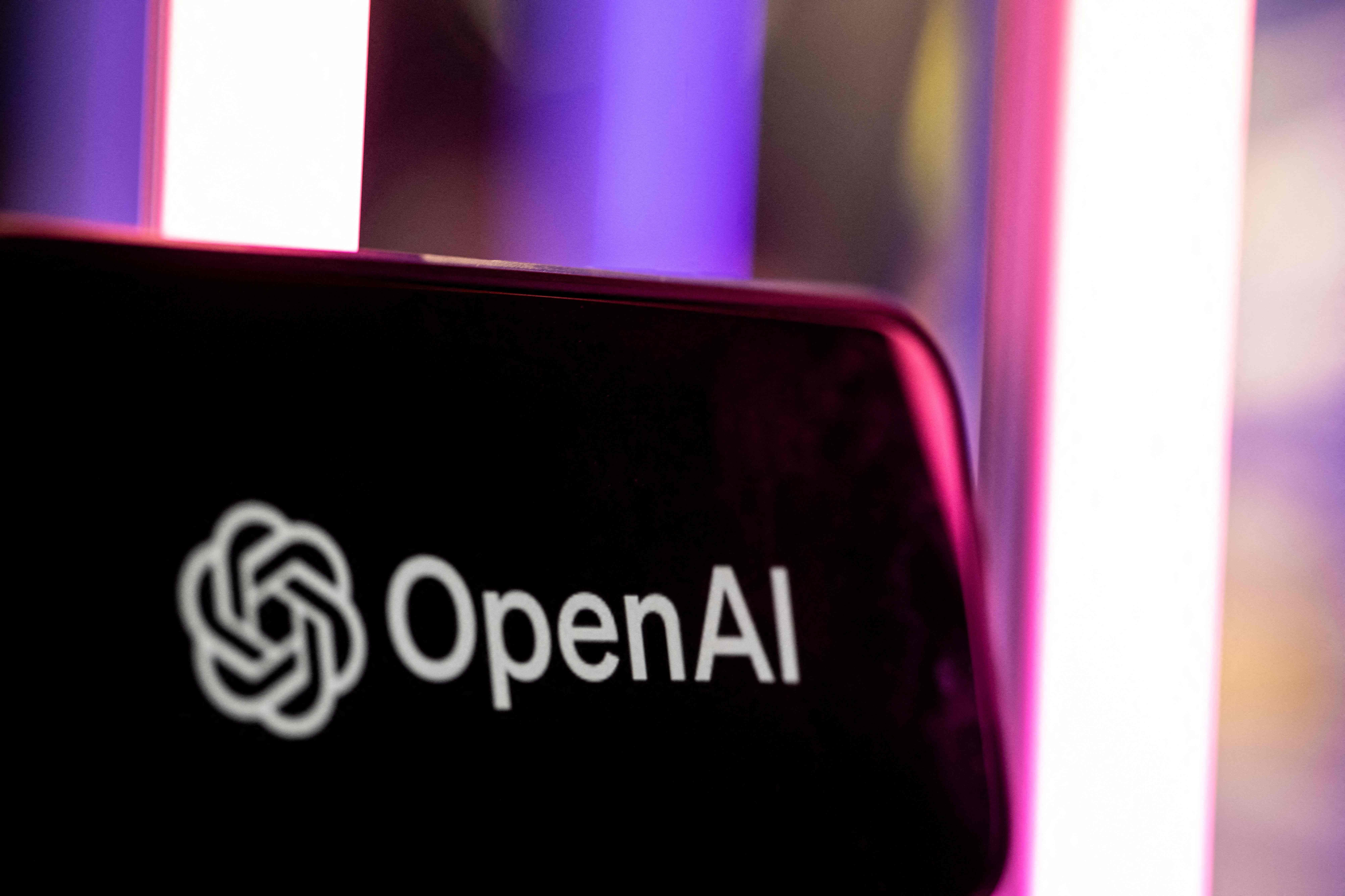 Das OpenAI-Logo auf einem Bildschirm vor unscharfem, bunt beleuchtetem Hintergrund.