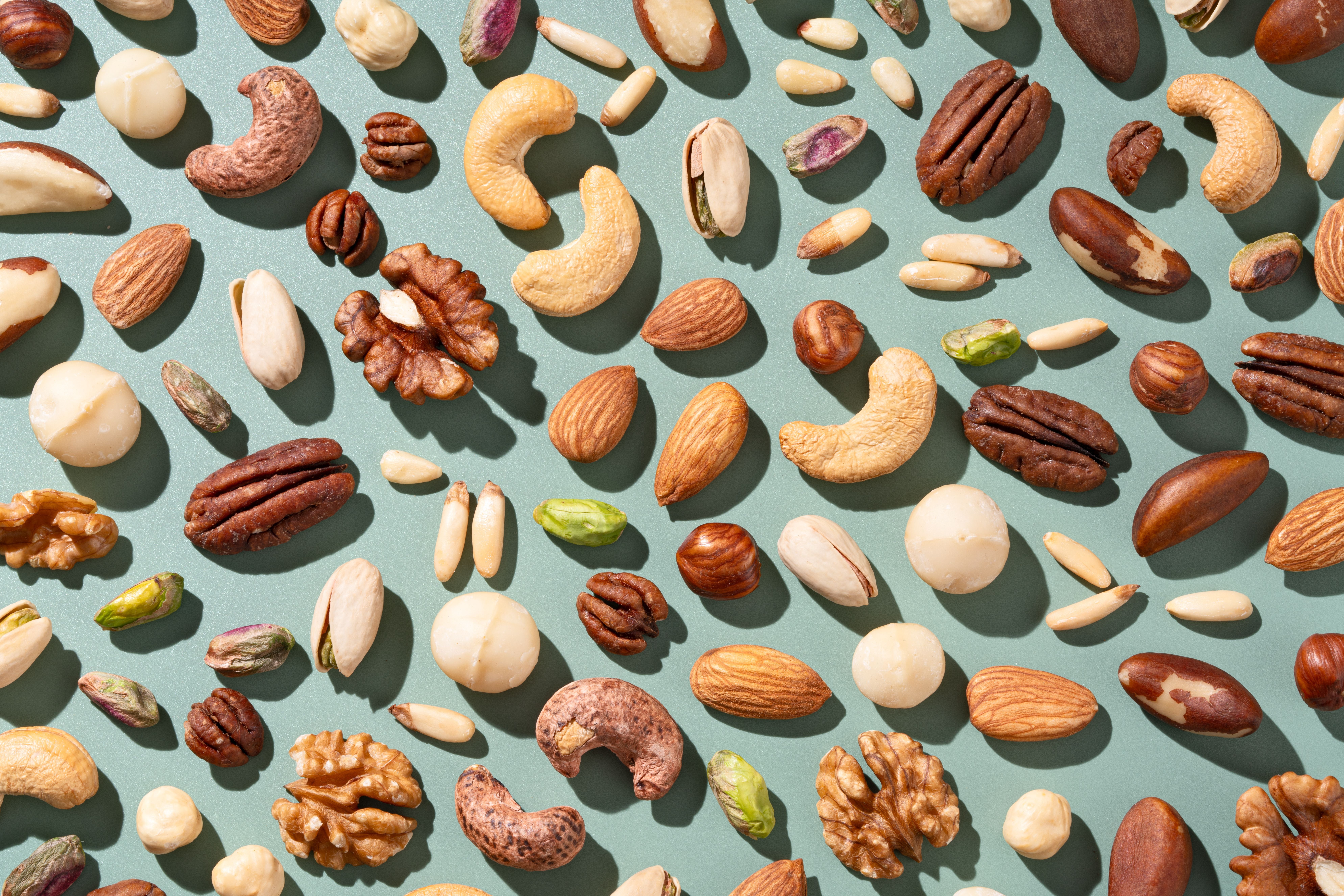 Verschiedene Nüsse wie Mandeln, Cashews, Walnüsse und Pistazien auf grünem Hintergrund verteilt.