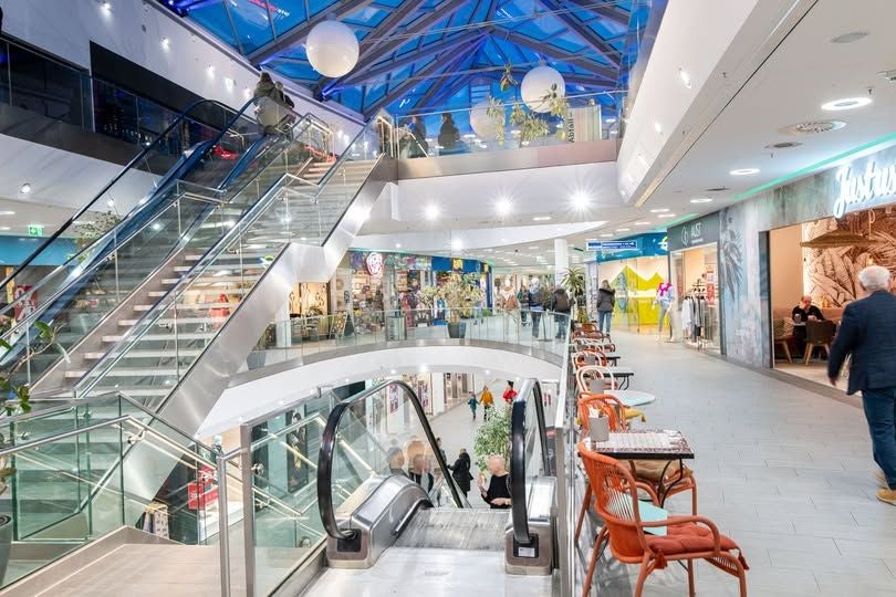 Helles Einkaufszentrum mit Rolltreppen, Glasdach und Cafétischen am Rand, Auhof Center.