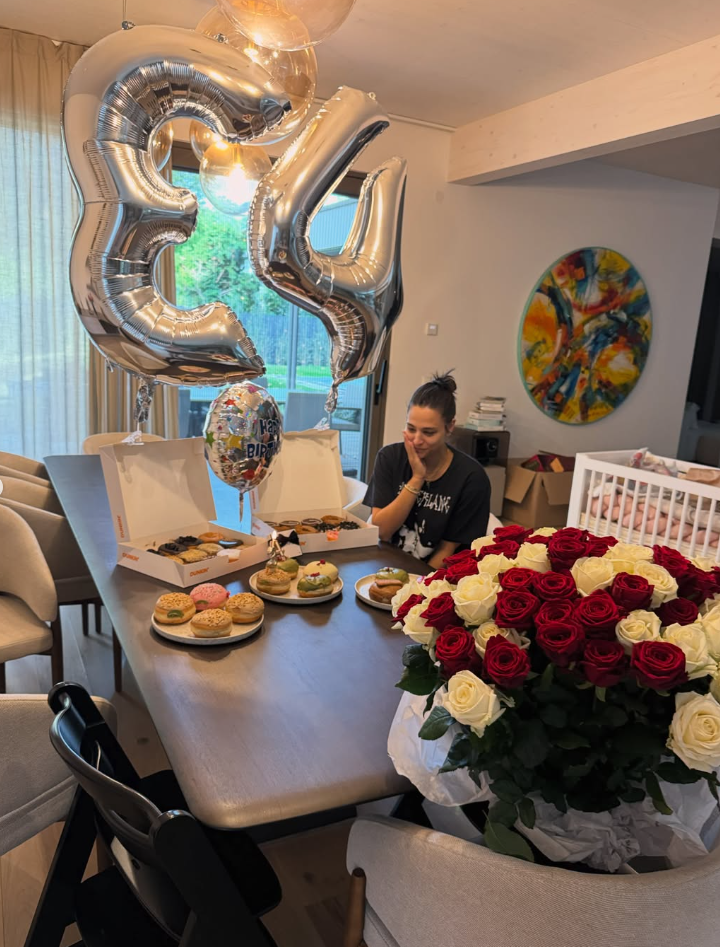 Frau sitzt am Tisch mit Donuts, großen Ballons mit der Zahl 34 und einem Strauß Rosen.
