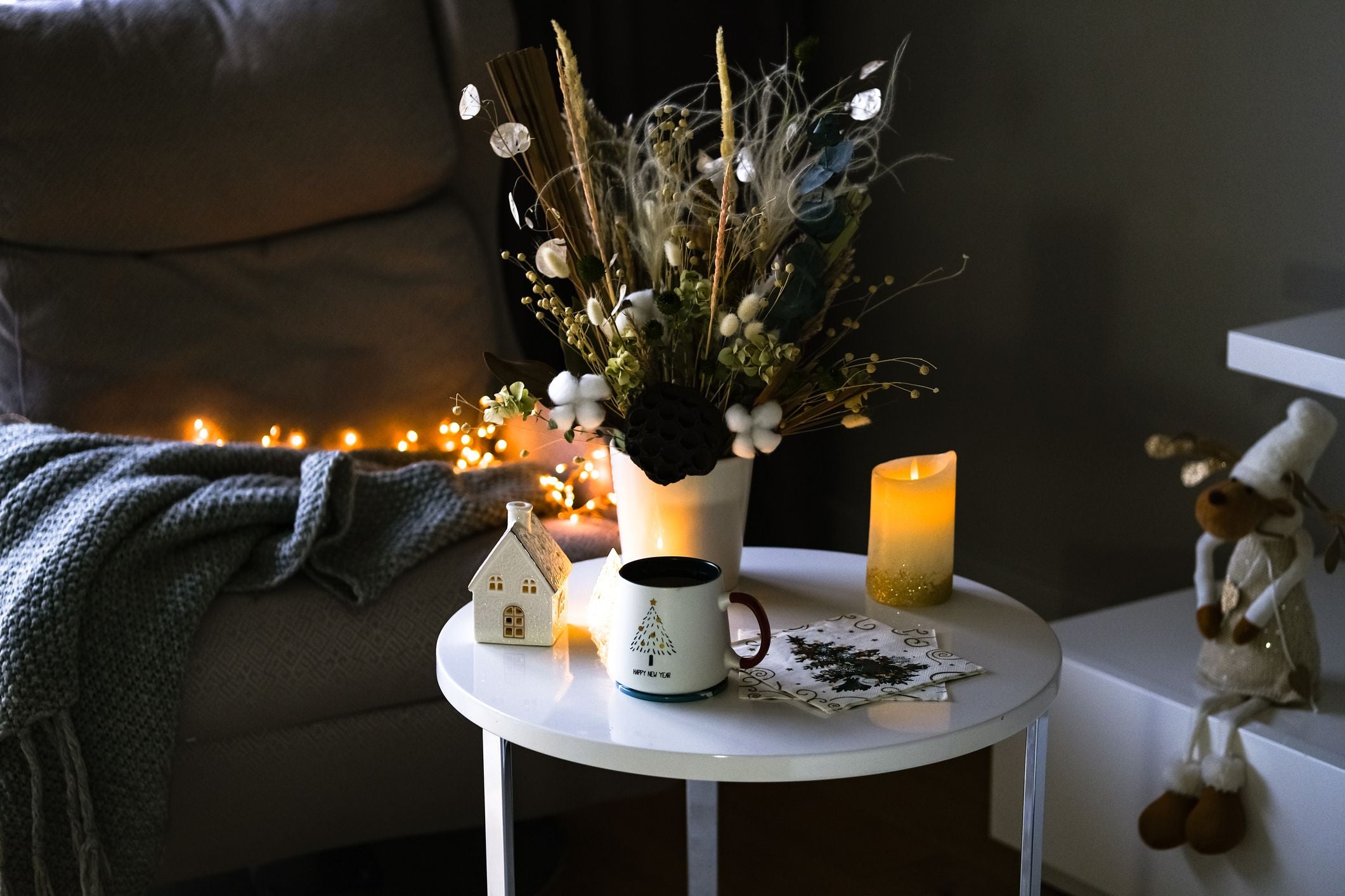 Gemütlich dekorierter Tisch mit Tasse, Kerze, Winterblumenstrauß und Lichterkette im Wohnzimmer.