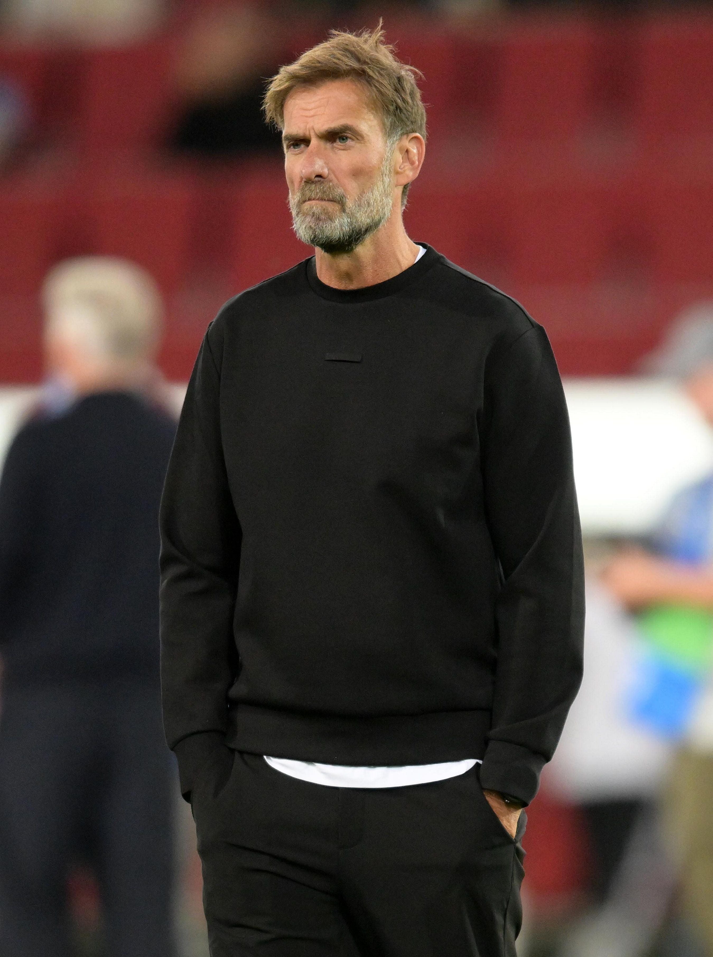 Ein Mann mit Bart und schwarzem Pullover steht auf einem Fußballfeld und schaut ernst.