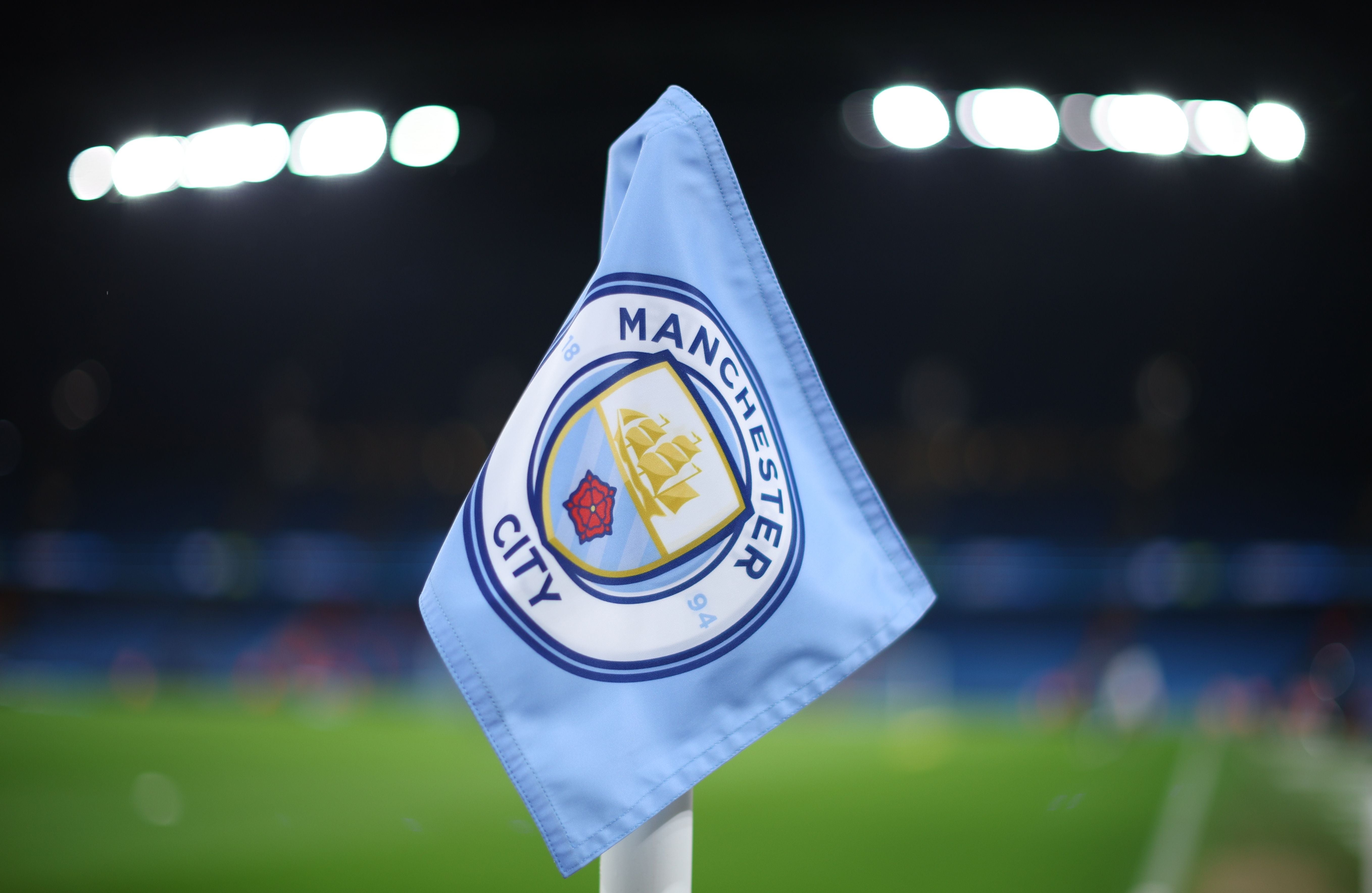 Eckfahne mit Manchester City Logo im Etihad Stadium, unscharfer Hintergrund bei Nacht.