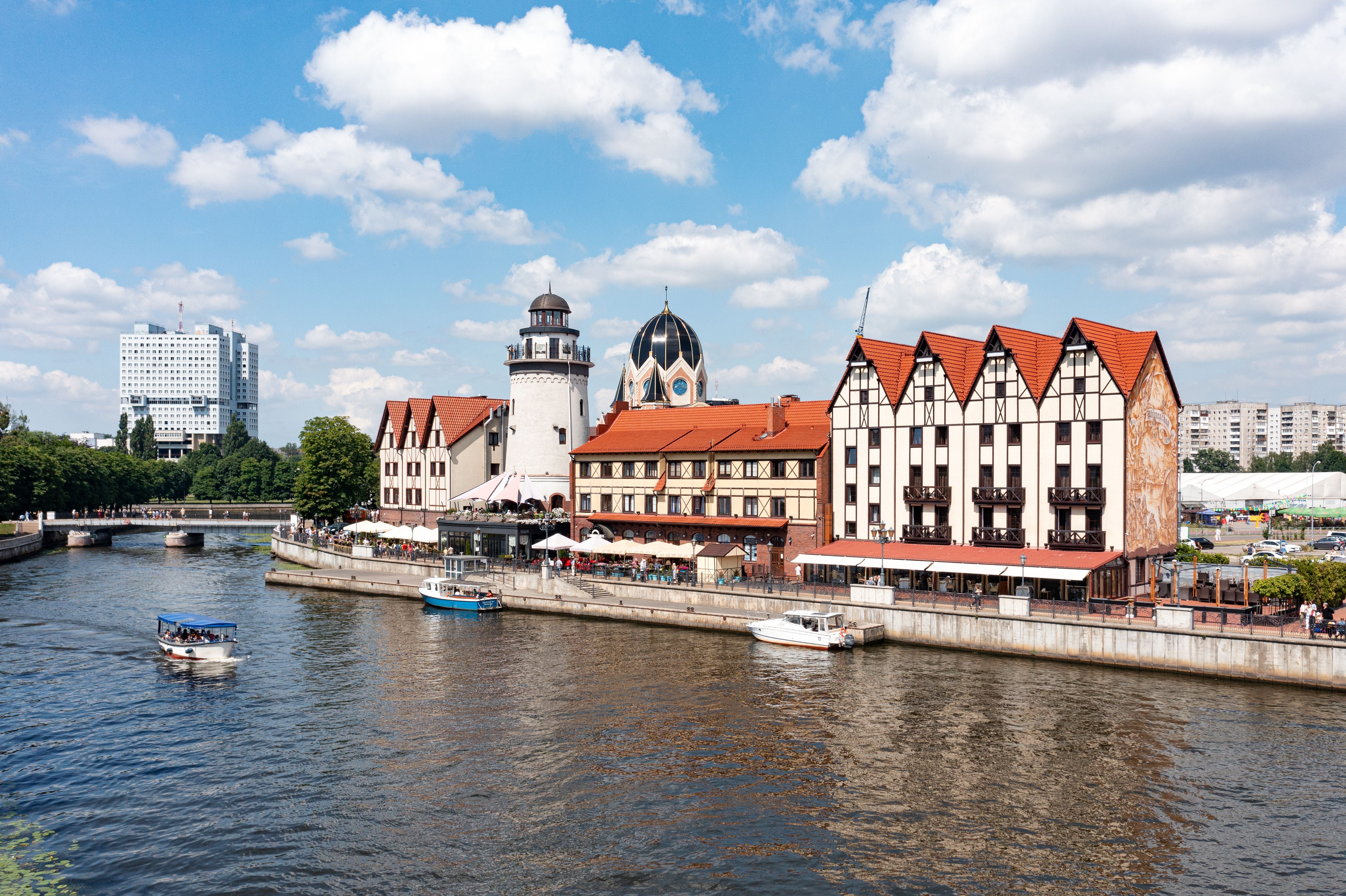 Fischerdorf in Kaliningrad am Fluss mit Fachwerkhäusern, Booten und blauem Himmel.