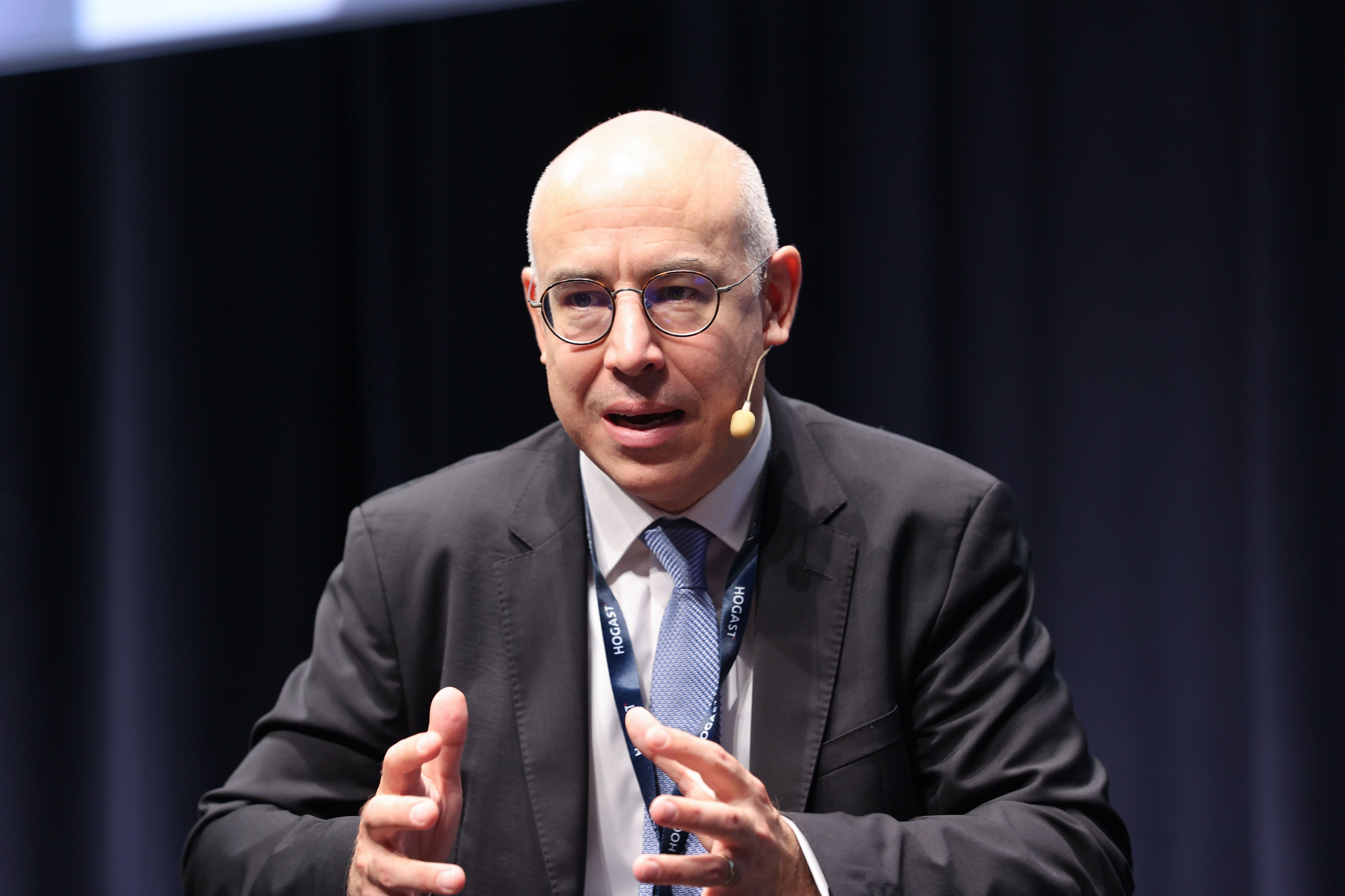 Ein Mann im Anzug spricht mit Mikrofon auf einer Bühne beim Symposium im Salzburg Congress.