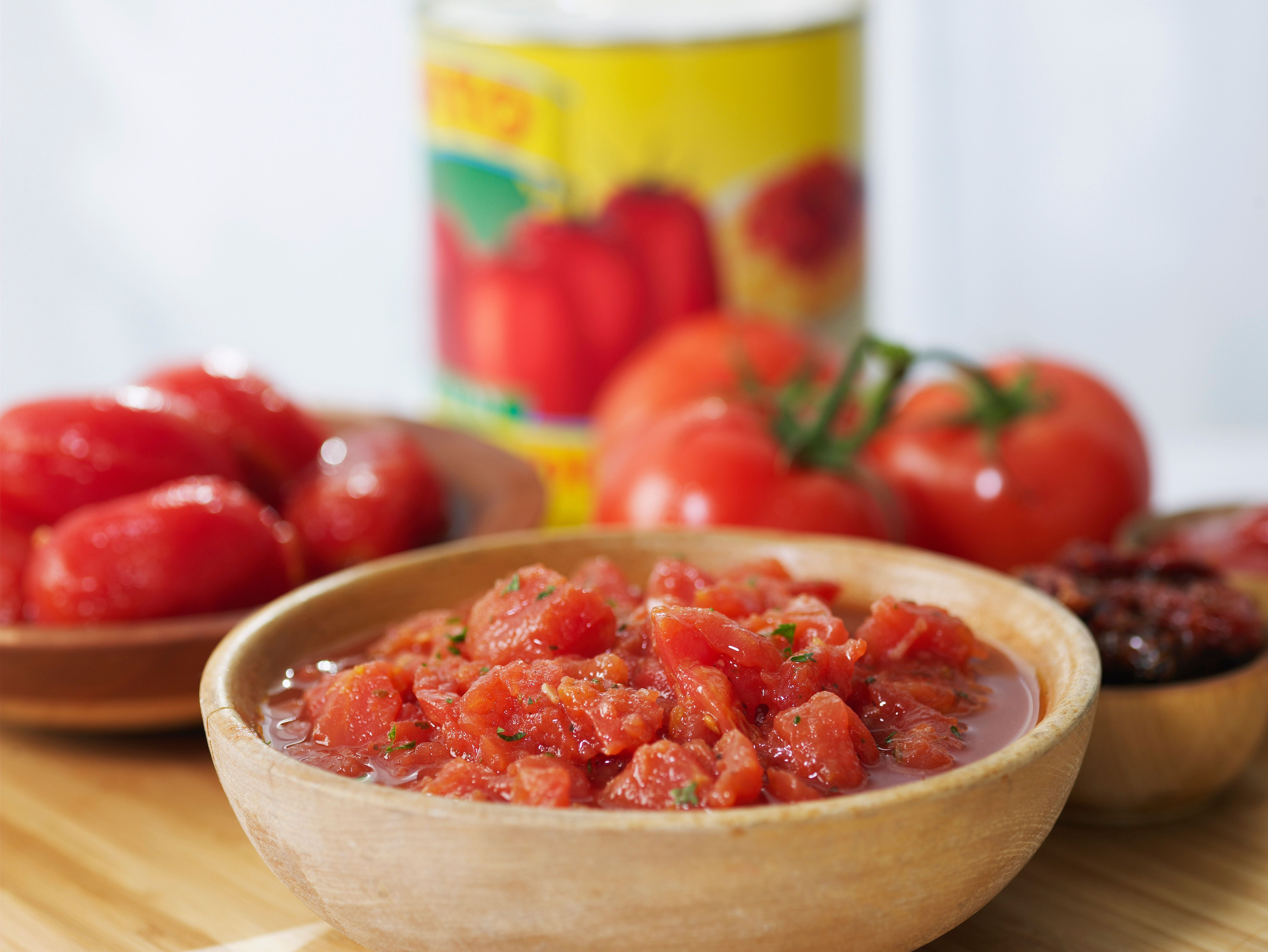 Schüssel mit gehackten Tomaten, daneben Tomaten am Strauch und weitere Tomatenprodukte.