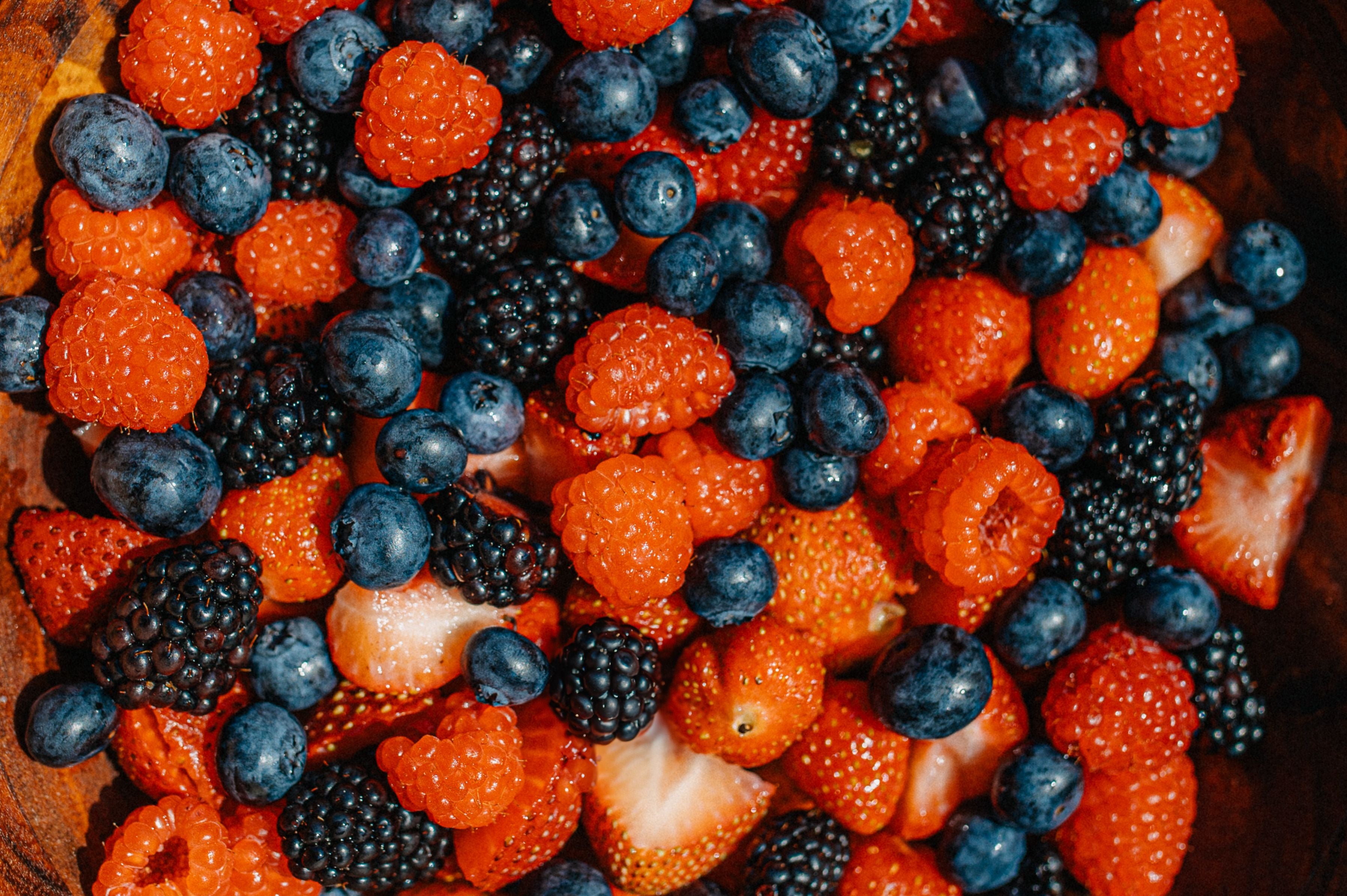 Verschiedene frische Beeren wie Erdbeeren, Blaubeeren, Himbeeren und Brombeeren liegen gemischt zusammen.