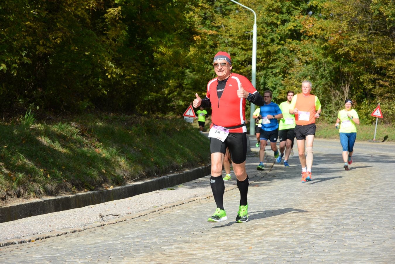 Mehrere Läufer laufen beim Wiener Höhenstraßenlauf auf einer sonnigen Straße im Freien.