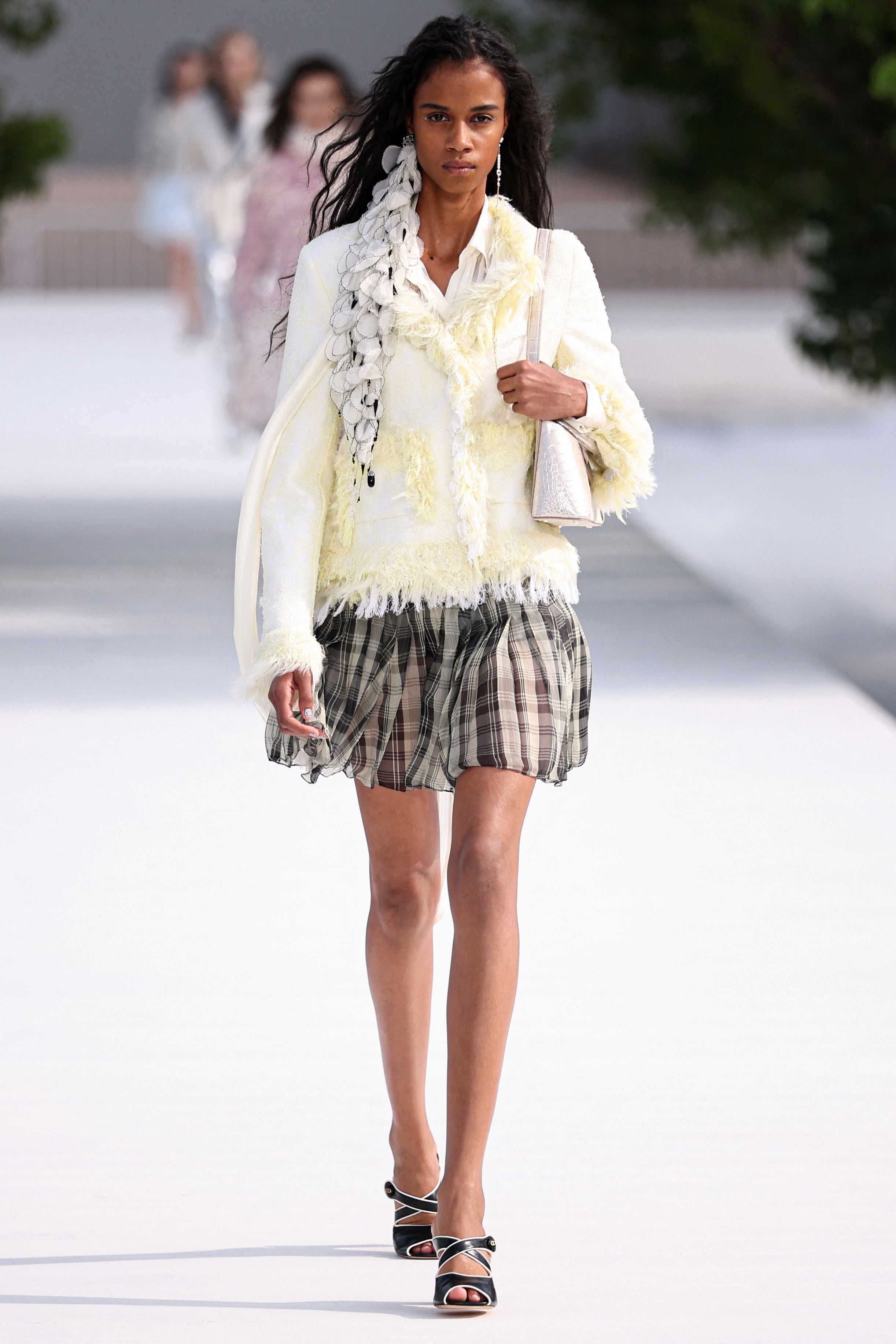 Model in hellem Jacket, karierter Rock und Sandalen auf dem Laufsteg bei einer Modenschau.