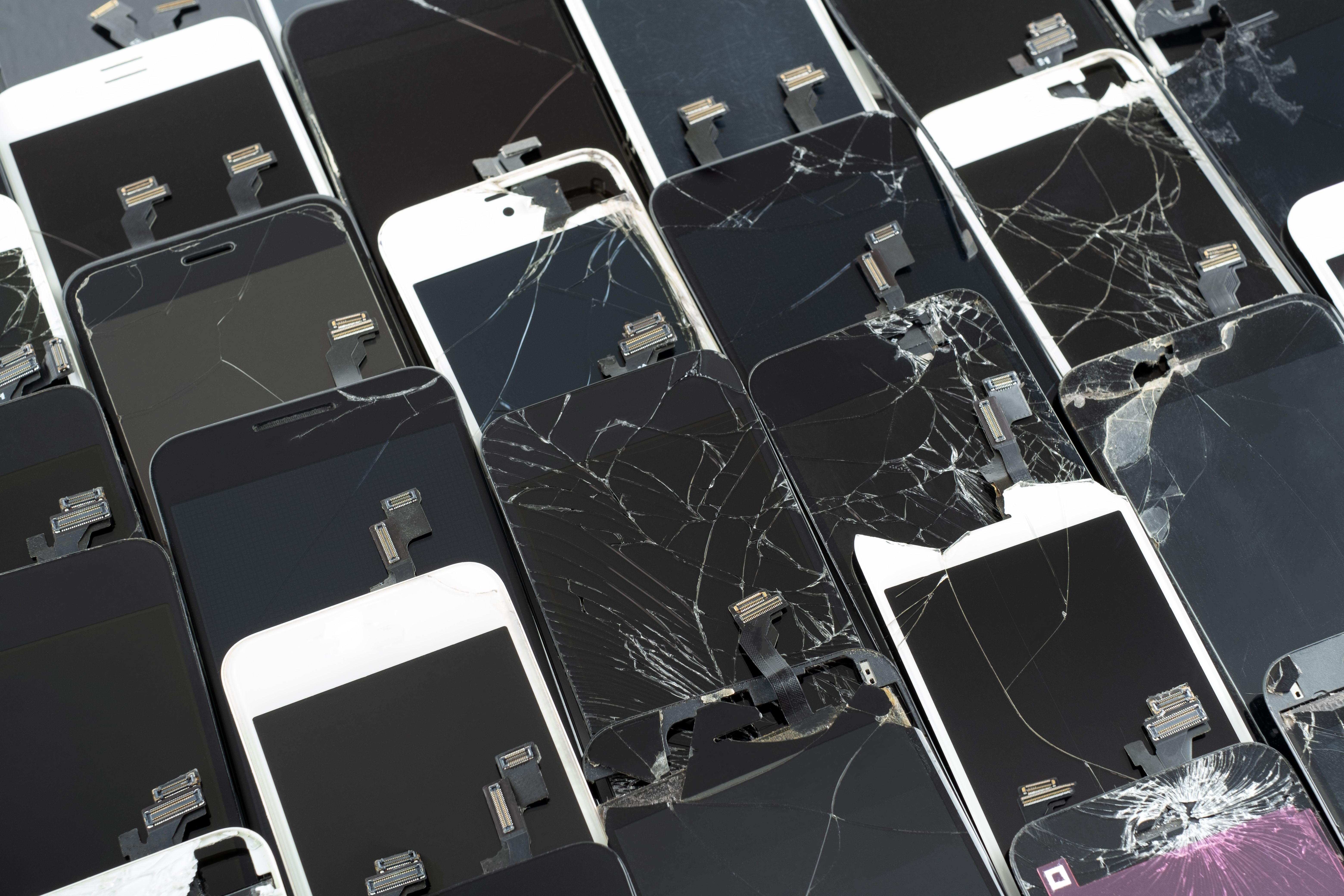 Mehrere kaputte Smartphone-Bildschirme liegen übereinander zur Wiederverwertung bereit.
