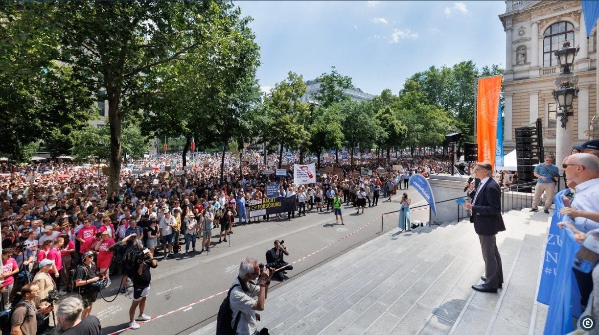 Große Menschenmenge protestiert vor der Universität Wien, der Direktor hält eine Rede auf den Stufen.