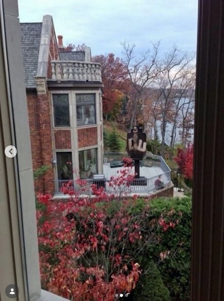 Blick aus dem Fenster auf eine Terrasse mit einer großen Mittelfinger-Skulptur im Garten.