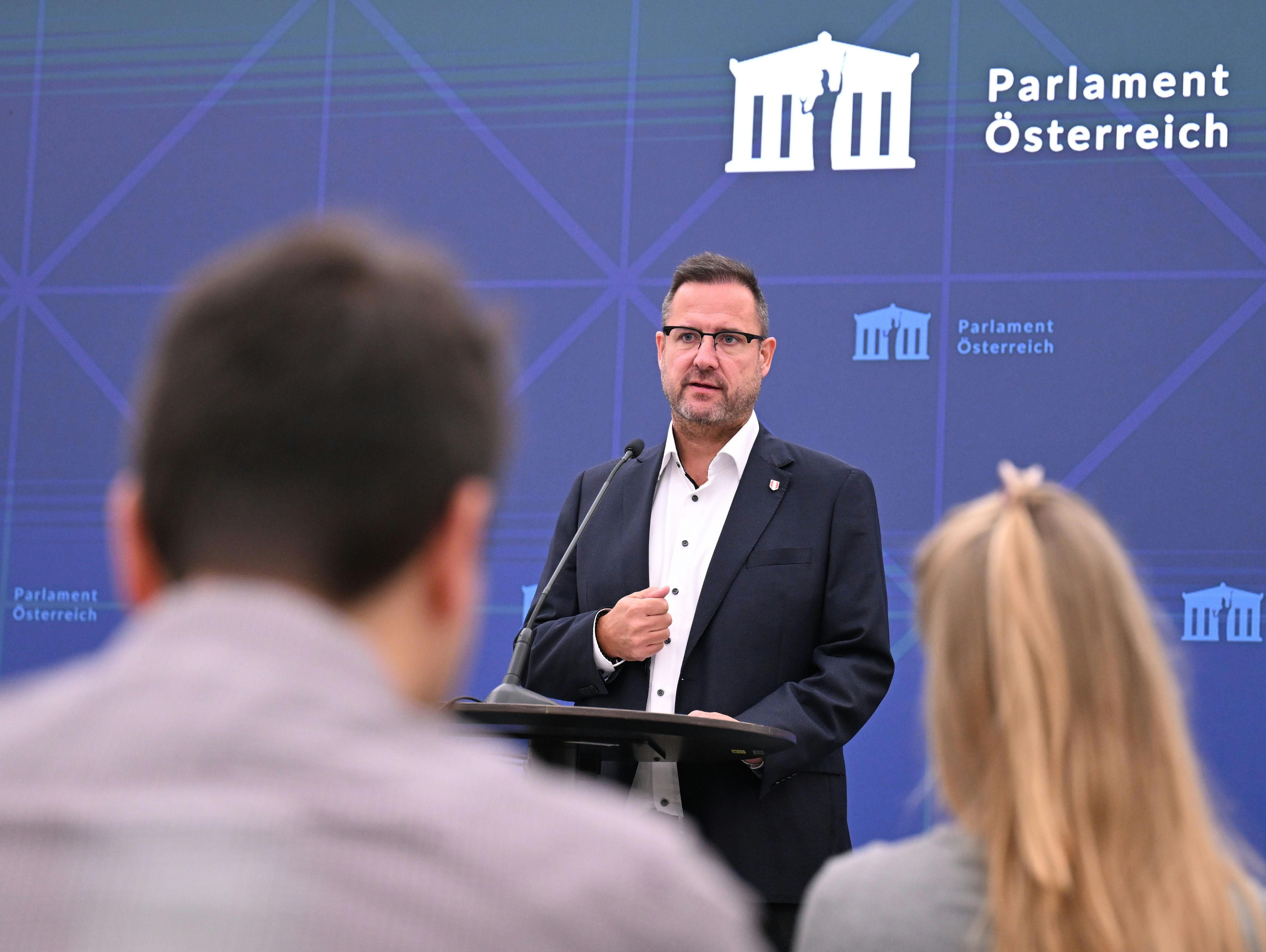 Ein Mann spricht bei einer Pressekonferenz im österreichischen Parlament vor Publikum.