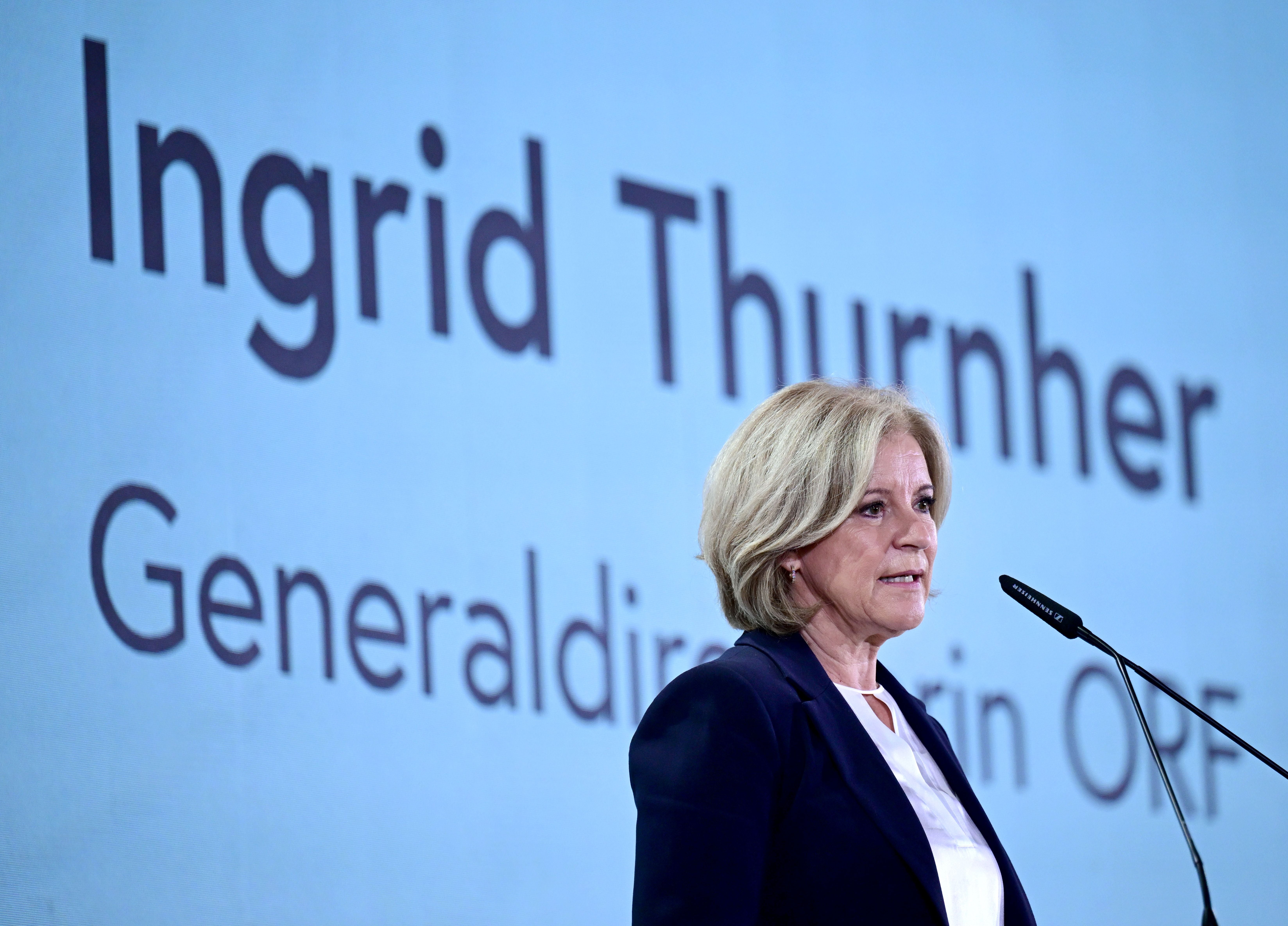 Eine Frau spricht am Rednerpult, hinter ihr steht groß "Ingrid Thurnher" an der Wand.