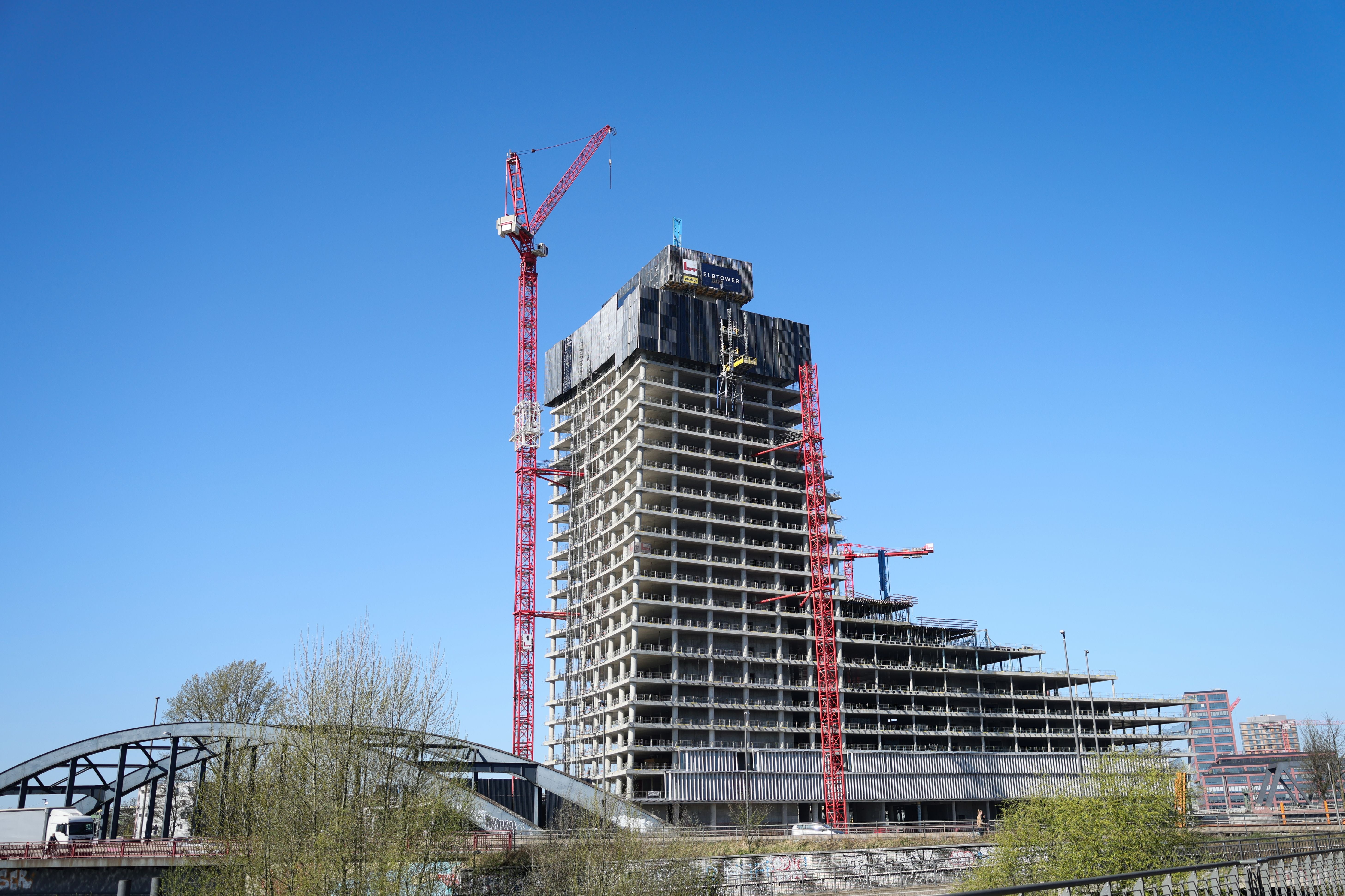 Unvollendeter Hochhausbau mit roten Kränen in Hamburg bei blauem Himmel, Elbtower im Rohbau.