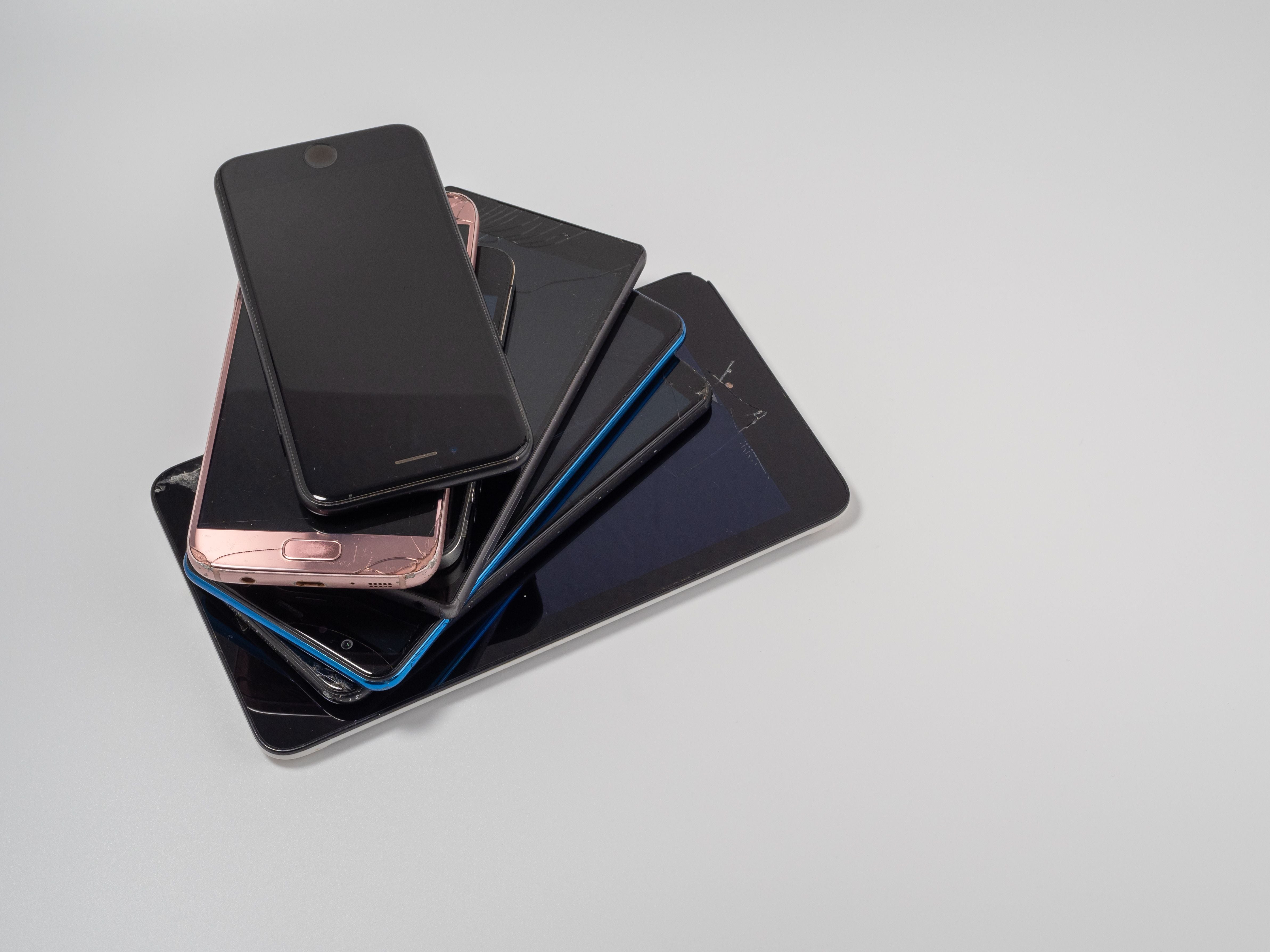 Mehrere kaputte Smartphones liegen übereinander auf einem hellen Hintergrund.