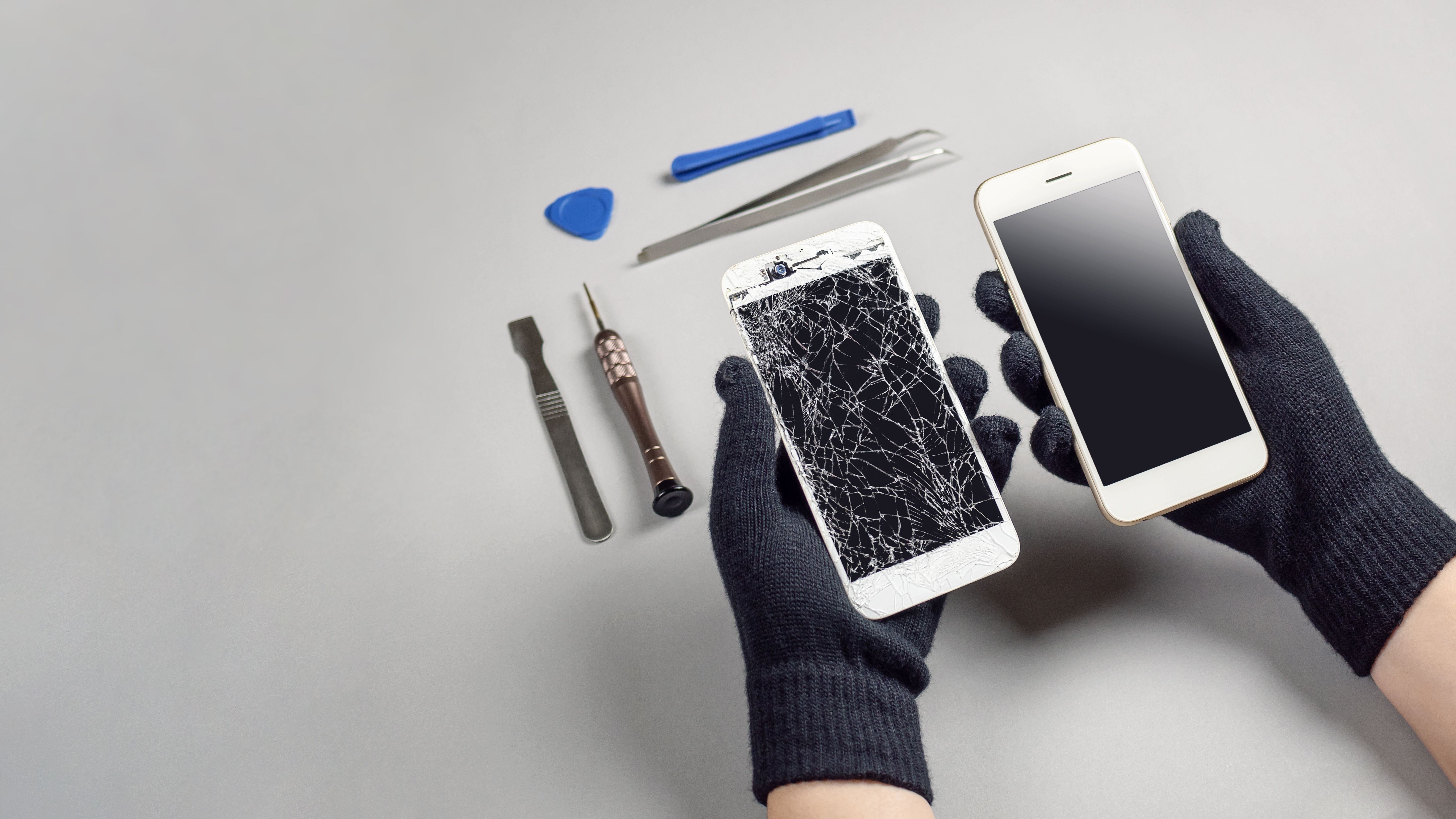 Zwei Hände halten ein kaputtes und ein intaktes Smartphone, daneben liegen Reparaturwerkzeuge.