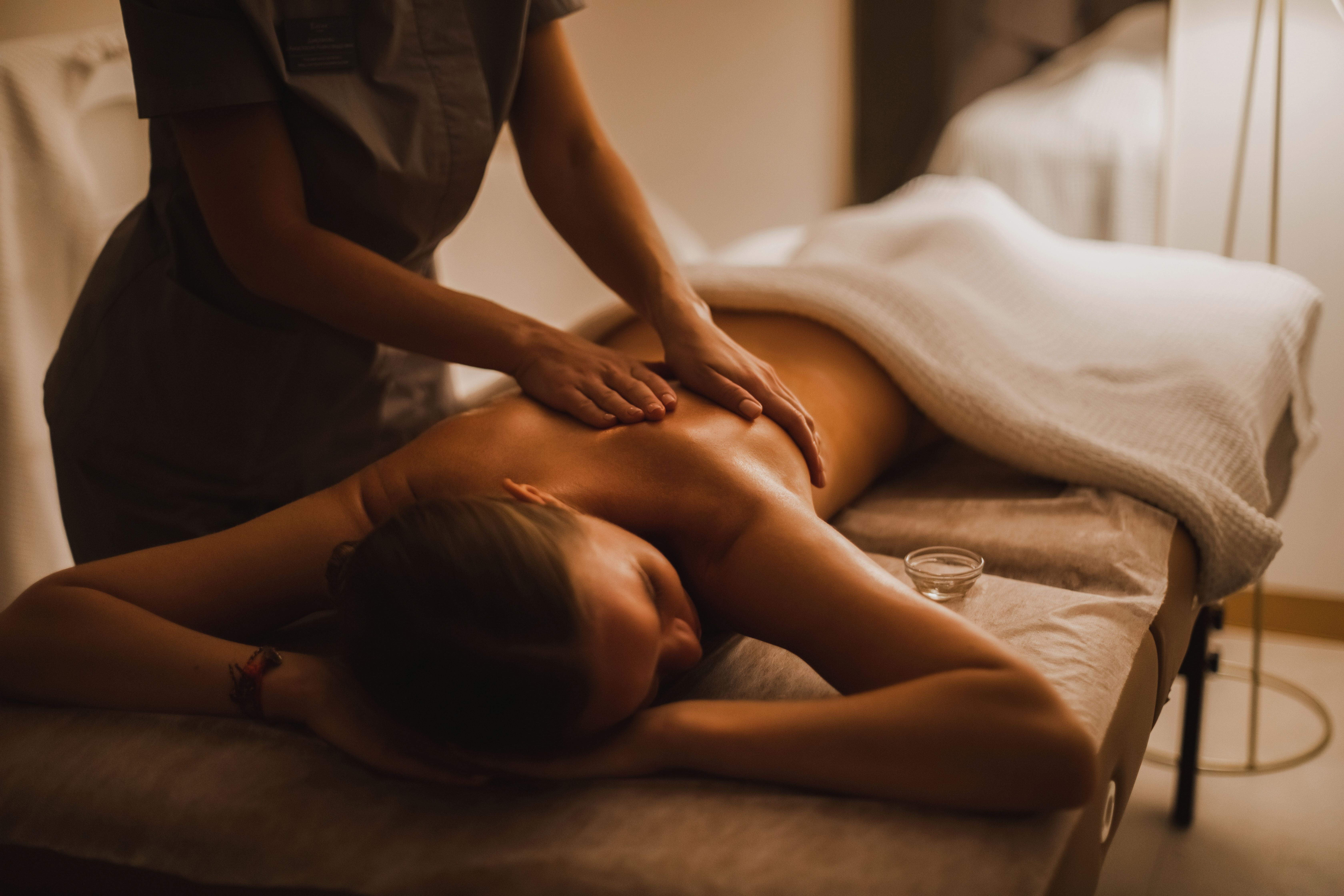 Eine Frau bekommt in einem Wellnessraum eine Rückenmassage von einer Masseurin.